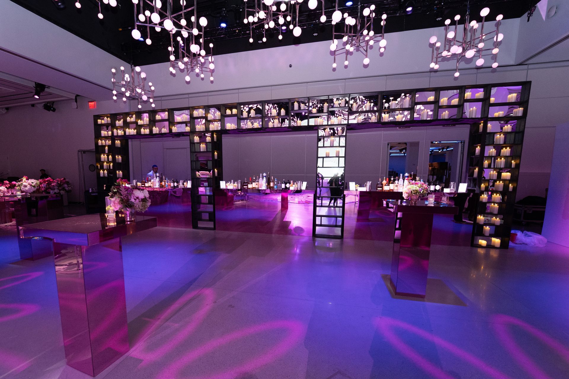 Elegant event hall with pink and purple lighting, tables, and candlelit archway.
