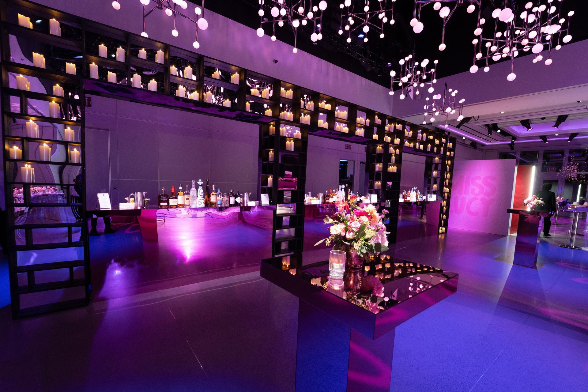 Event space bathed in purple light. Tables with products, ornate shelves with candles, and hanging lights.