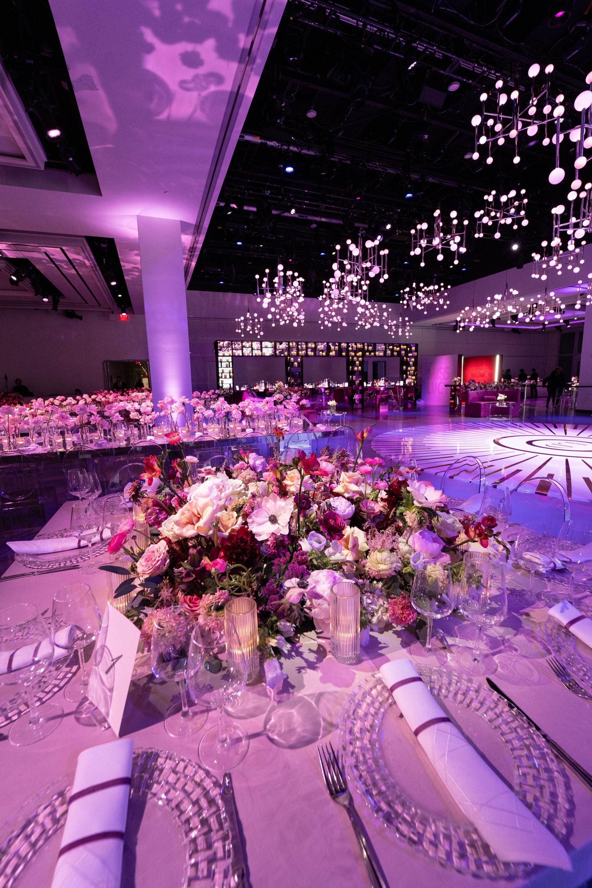 Elegant banquet hall with floral centerpieces, crystal place settings, and purple lighting.