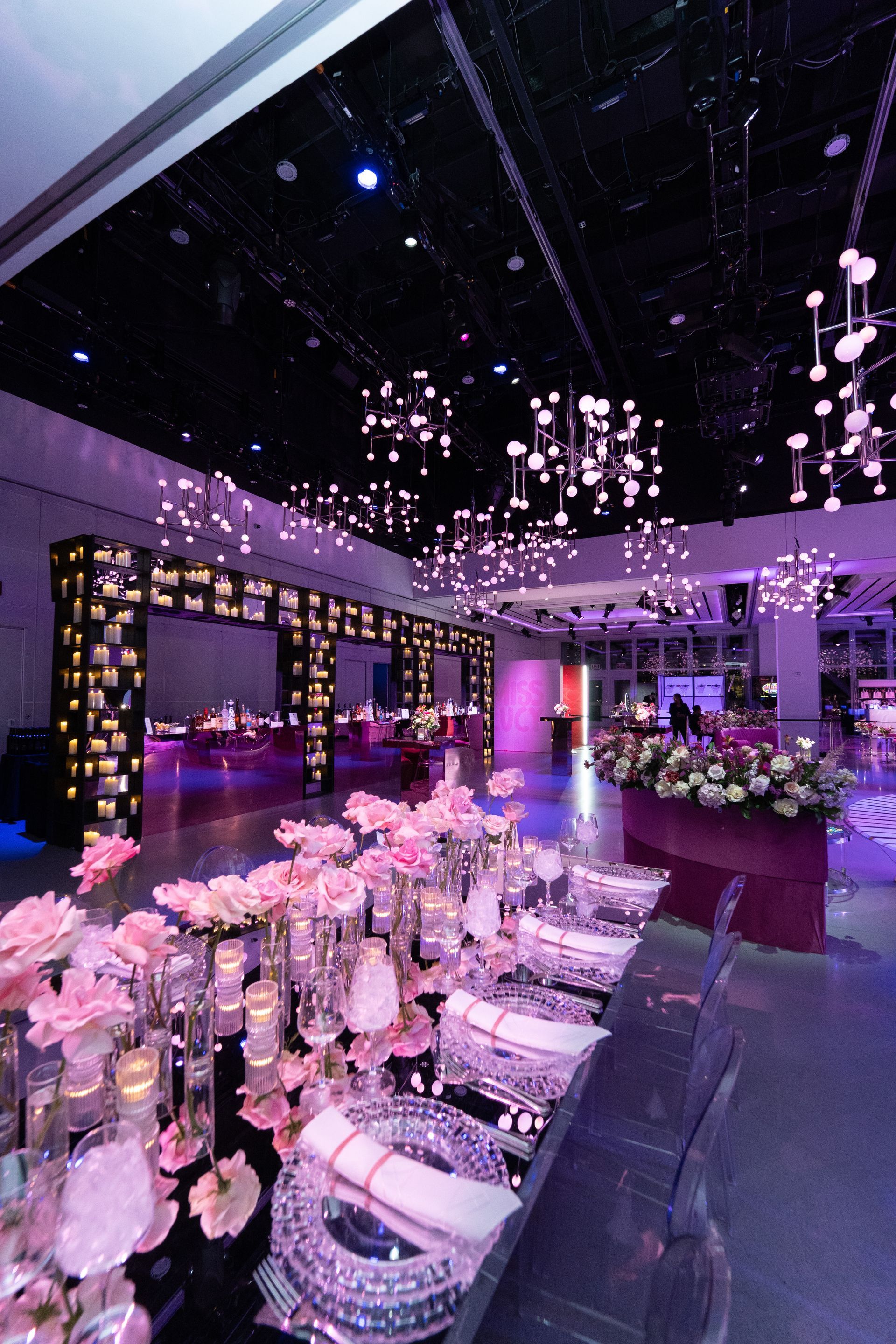 Elegant ballroom decorated for a formal event with pink floral arrangements, candles, and chandeliers.
