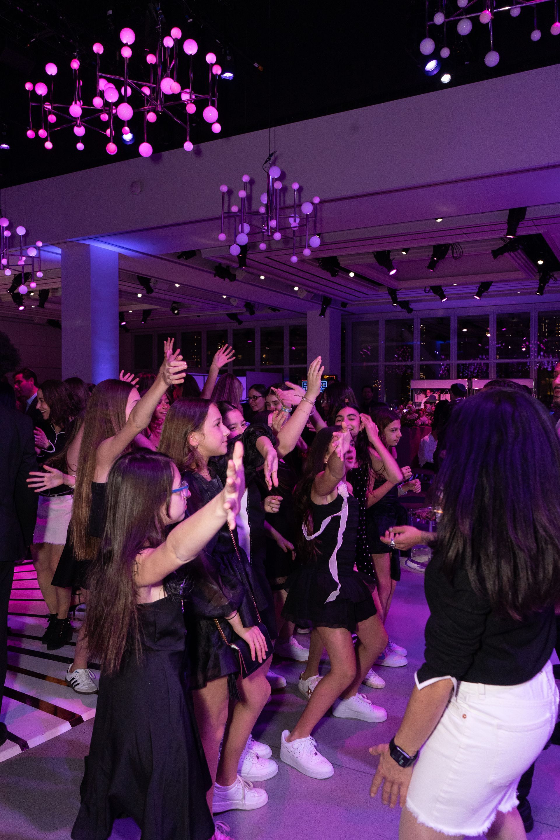 People dancing in a party setting. Purple lighting, girls wearing black outfits and white sneakers.