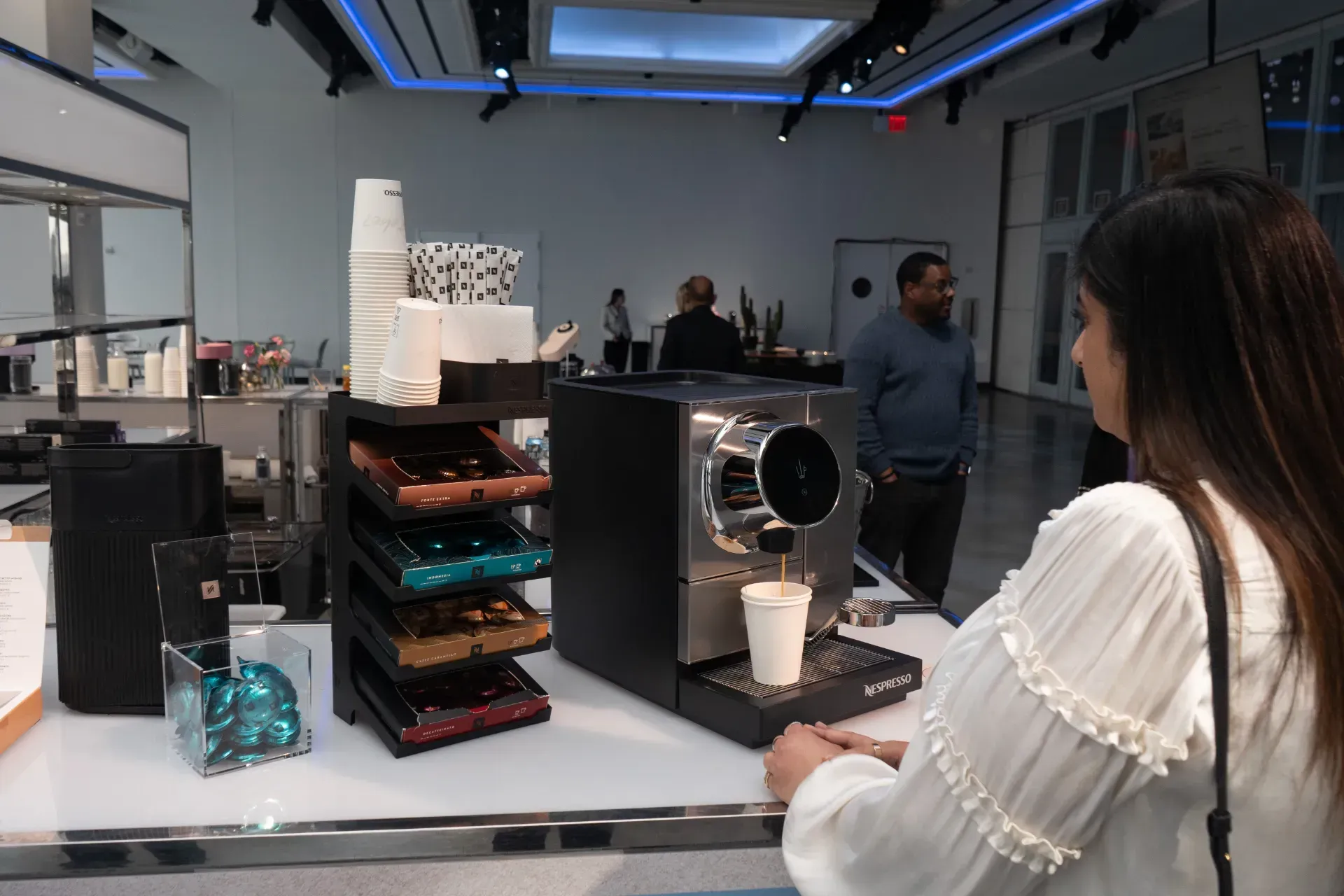 A woman in a white shirt is standing in front of a coffee machine.