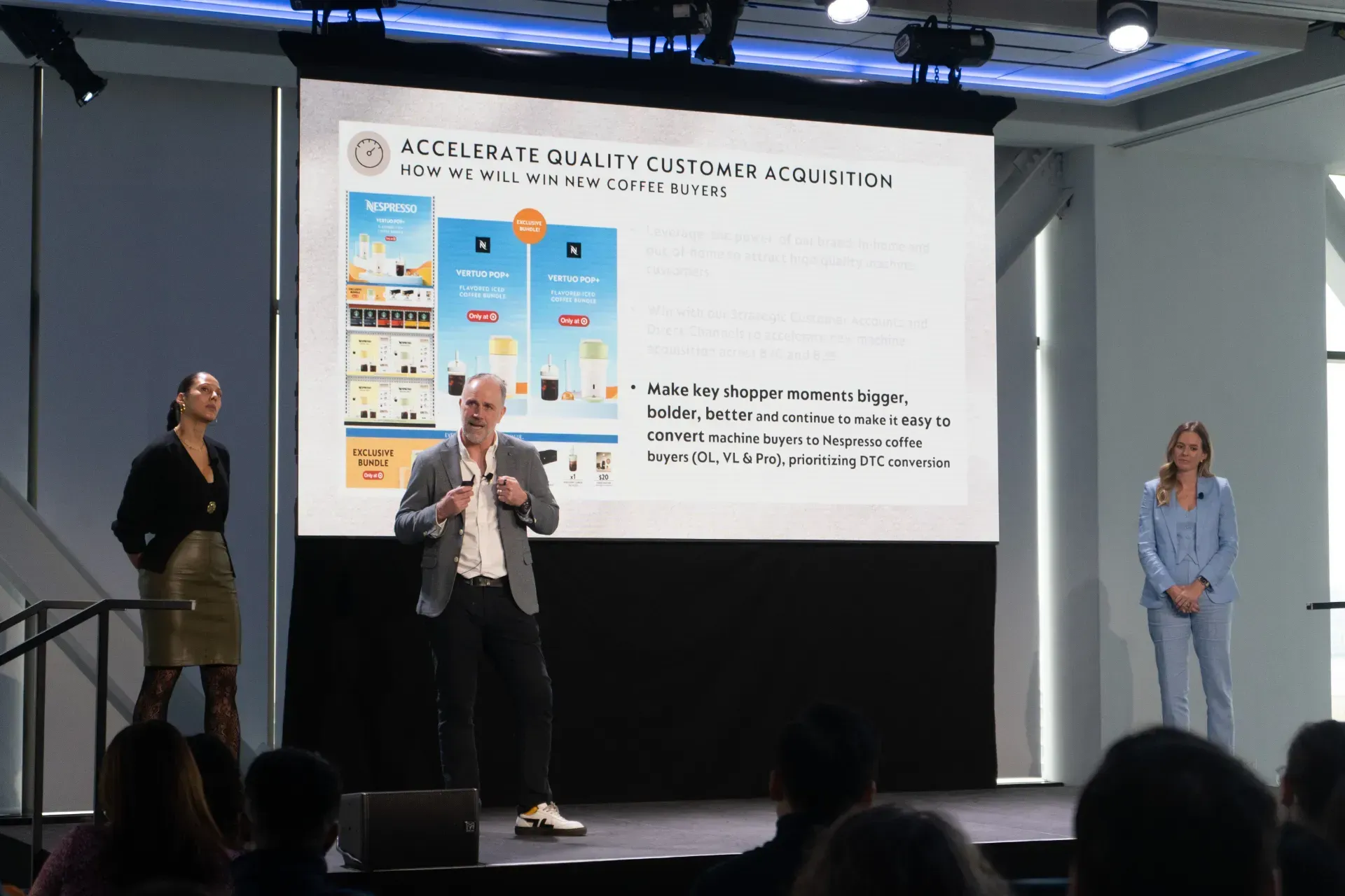 A man is giving a presentation on a stage in front of a large screen.