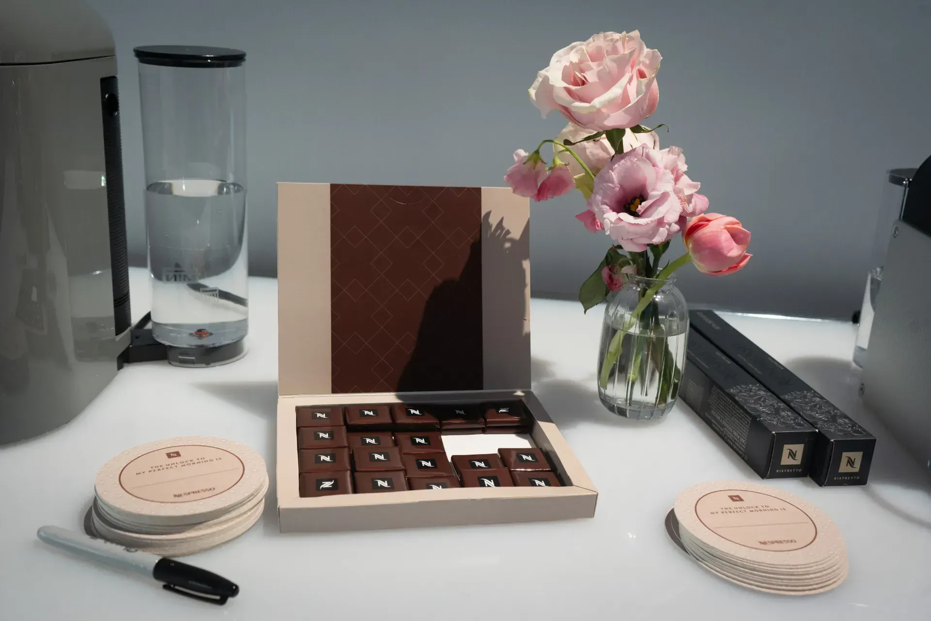 A box of chocolates sits on a table next to a vase of flowers