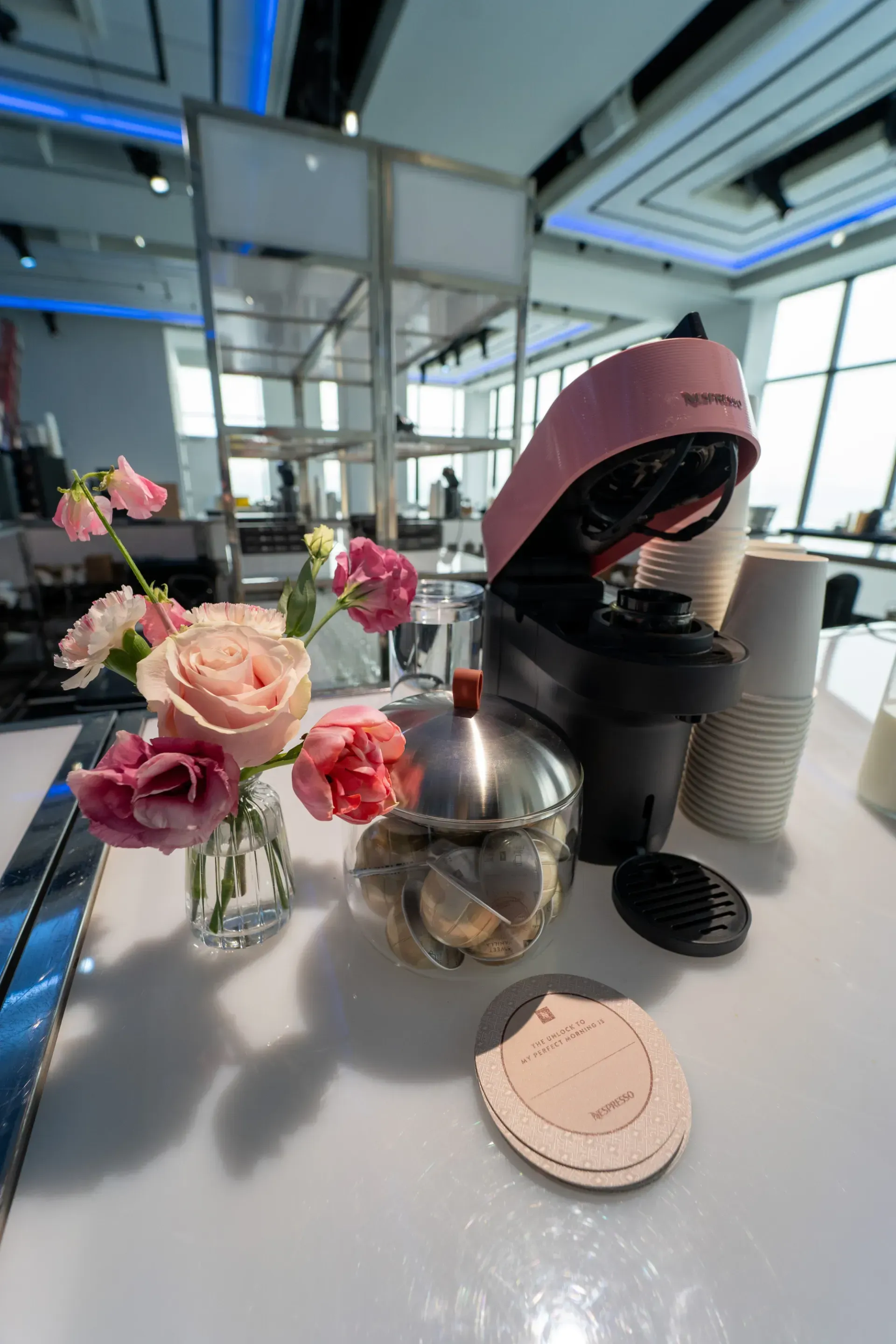 A pink coffee maker is sitting on a counter next to a vase of flowers.