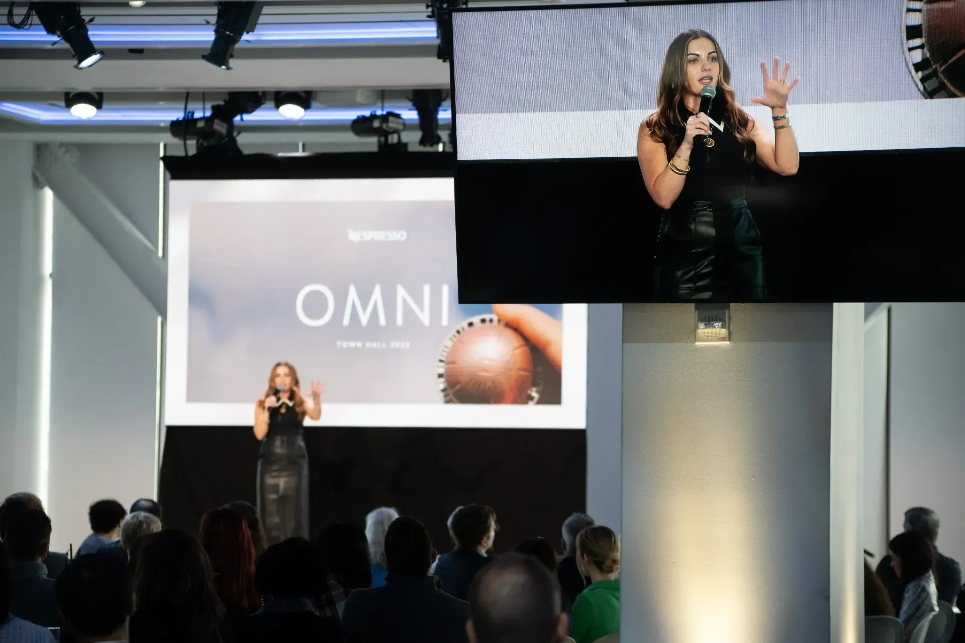 A woman is standing in front of a large screen with the word omni on it.