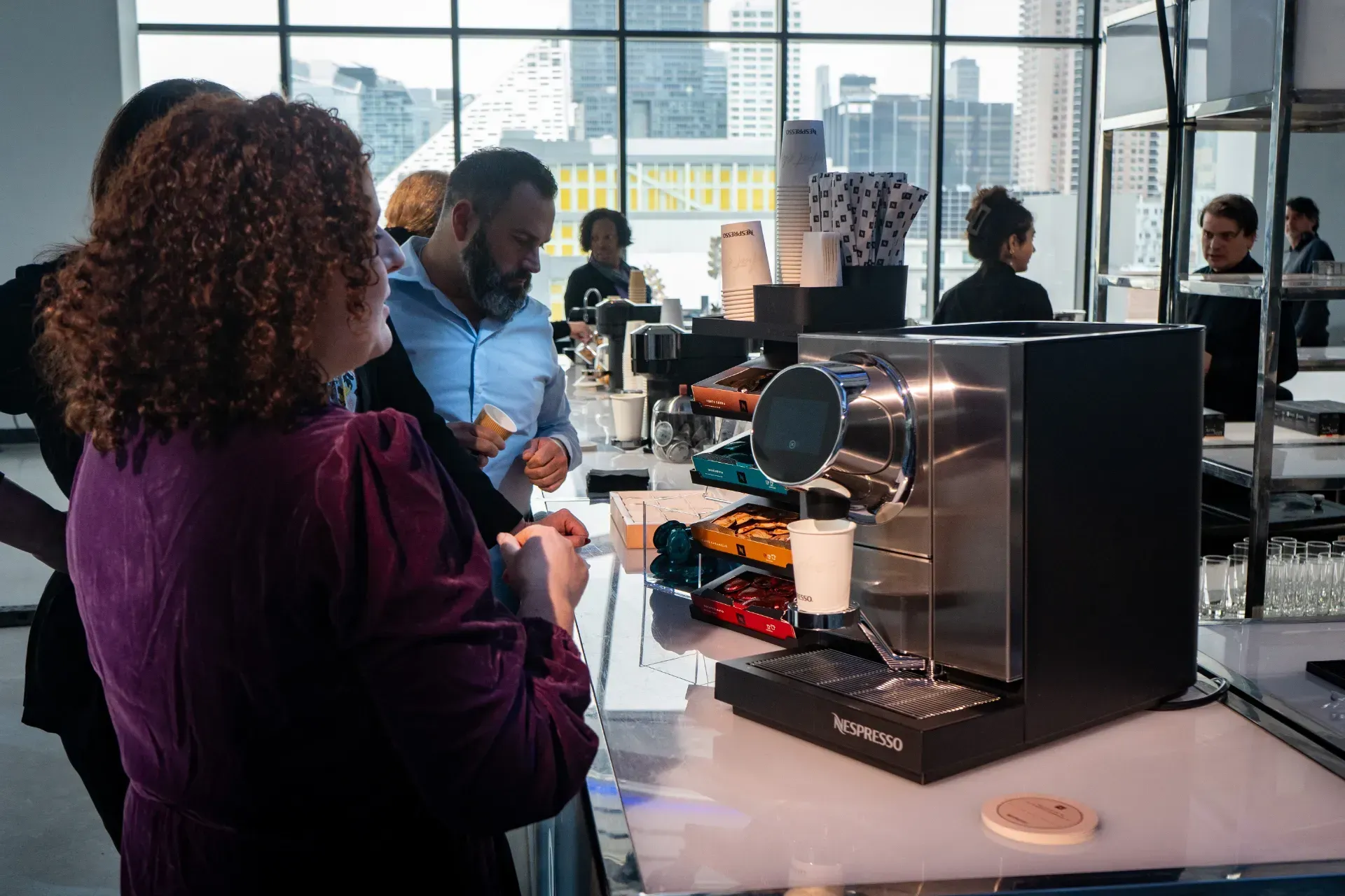 A group of people are standing around a counter looking at a coffee machine.