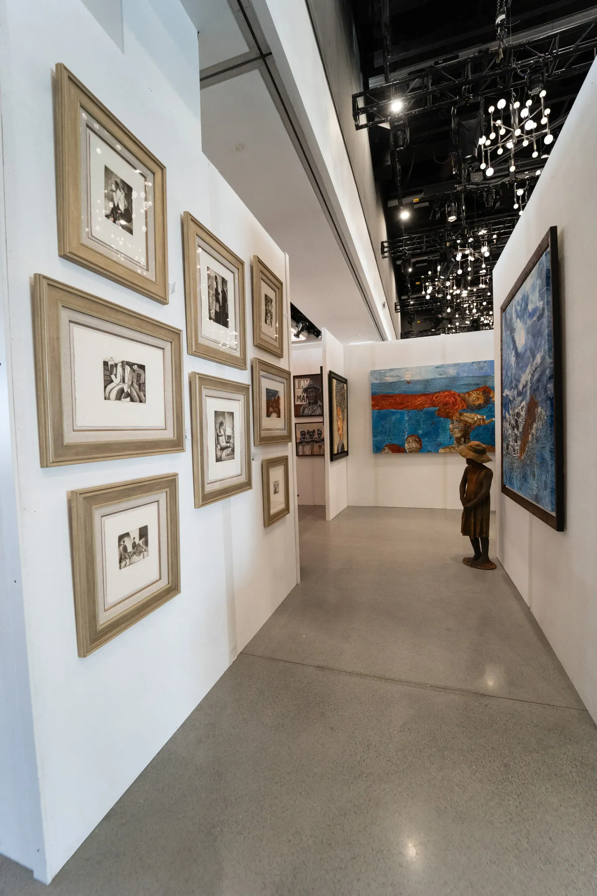 A hallway filled with paintings and a statue of a man in a hat.