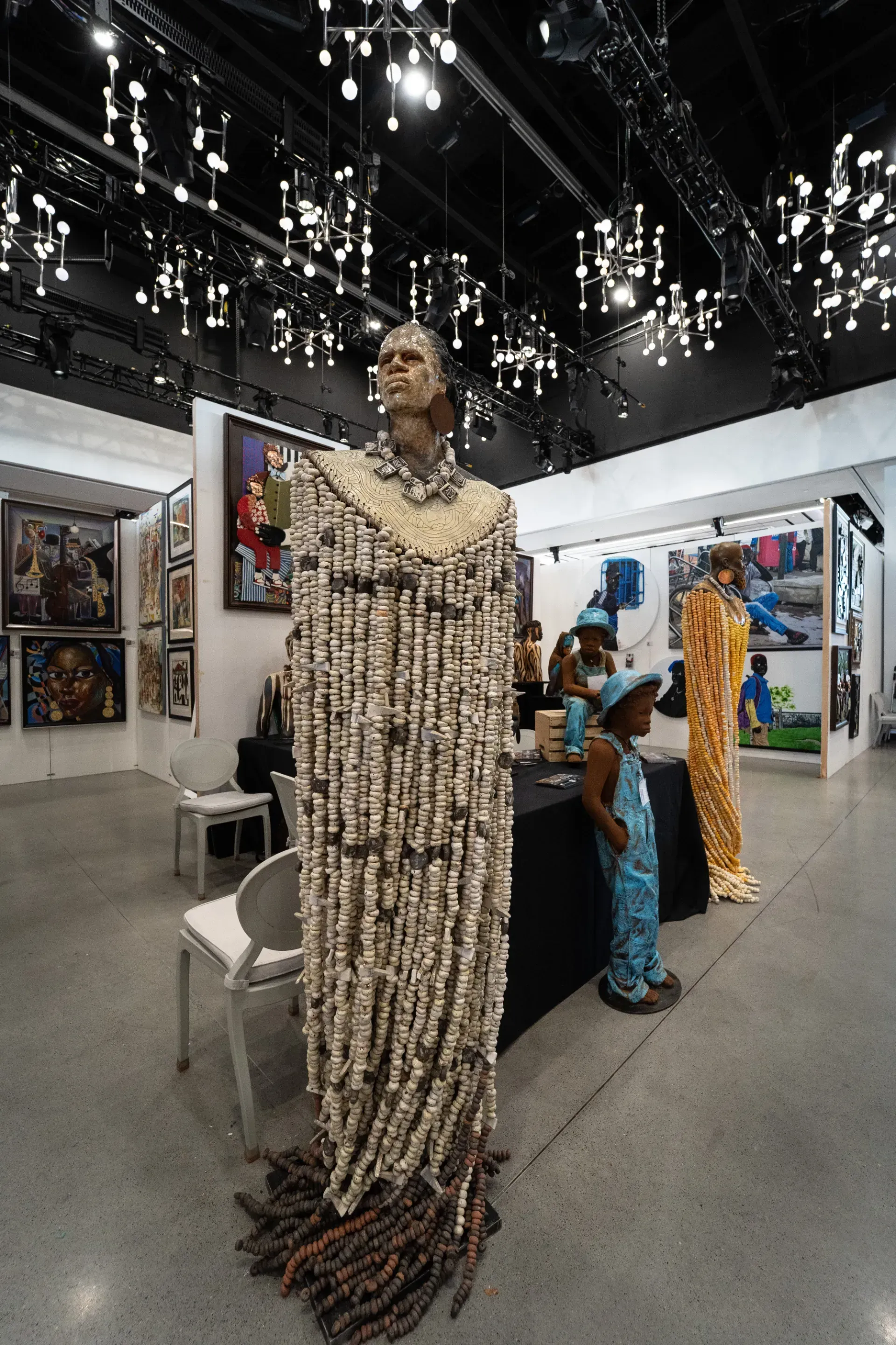 A statue of a woman made of beads is sitting in a room with other sculptures.
