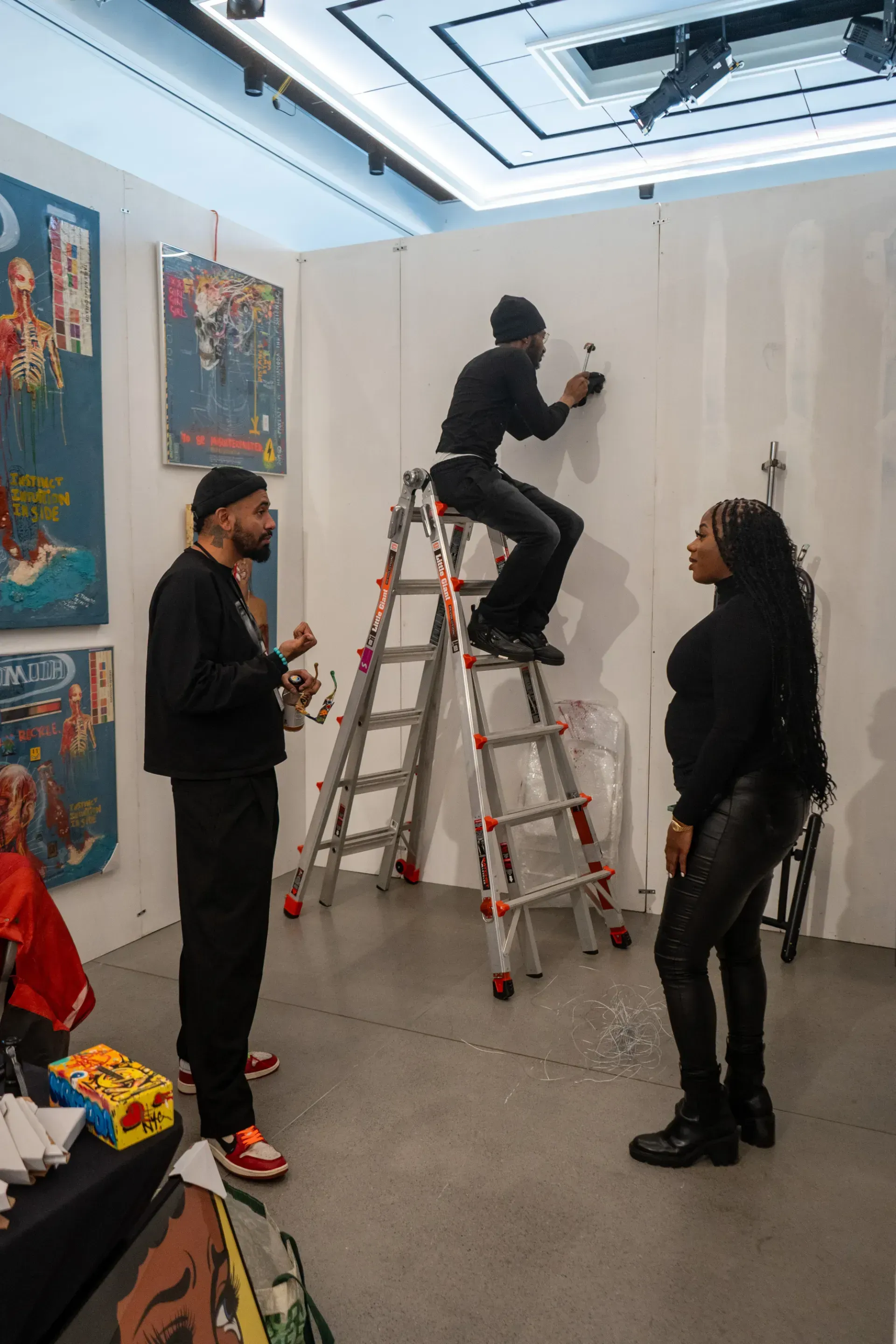 A man is sitting on a ladder painting a wall while a woman stands next to him.