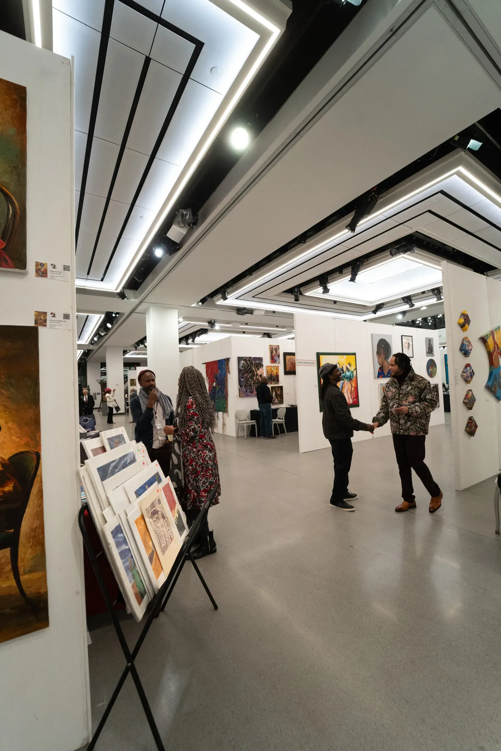 A group of people are standing in a room with paintings on the walls.