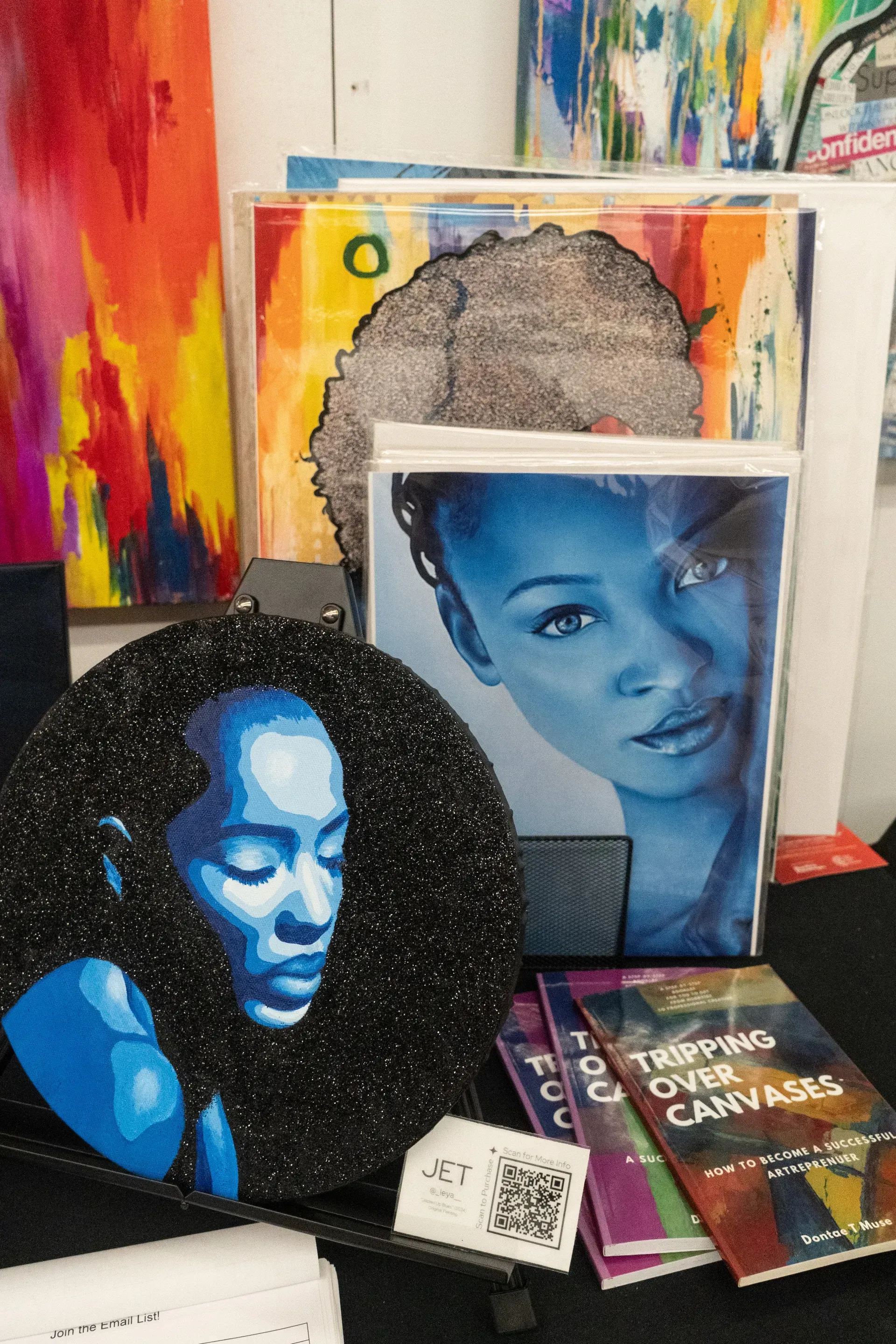 A painting of a woman 's face is on a table with other paintings.