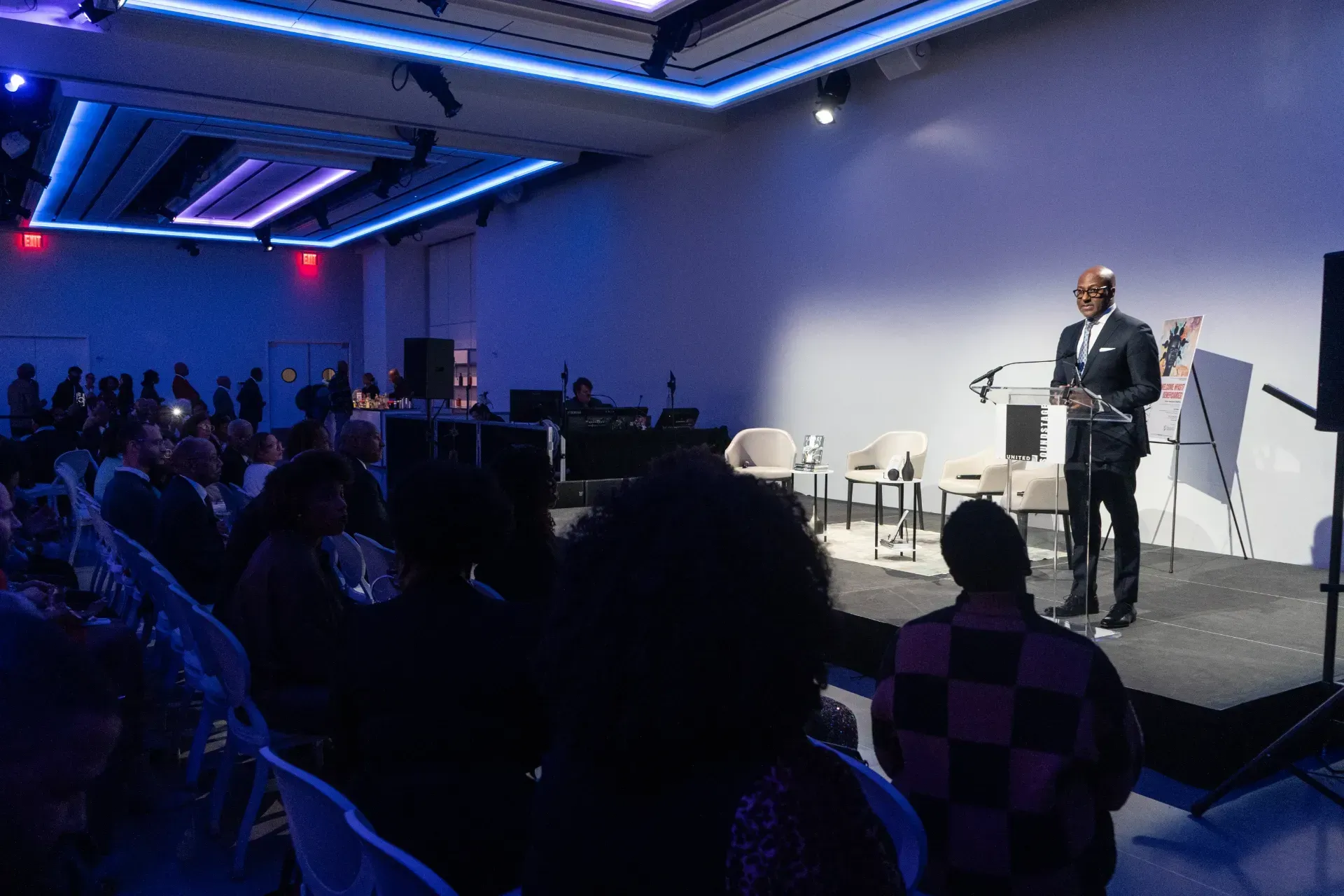 A man is standing on a stage giving a speech to a crowd of people.