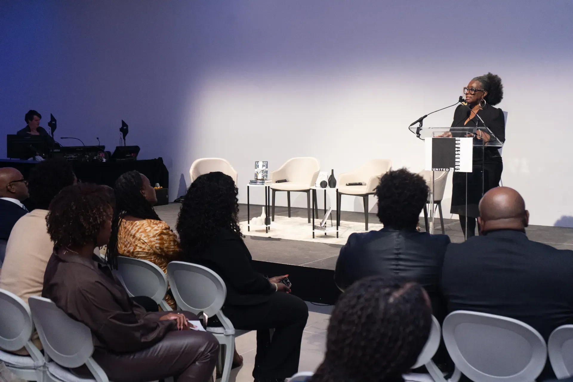 A woman is standing at a podium giving a speech to a group of people sitting in chairs.