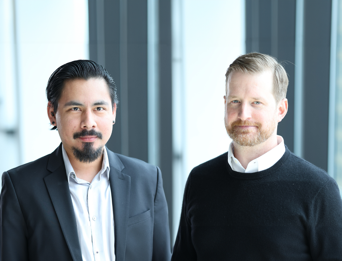 Two men are standing next to each other in front of a window.