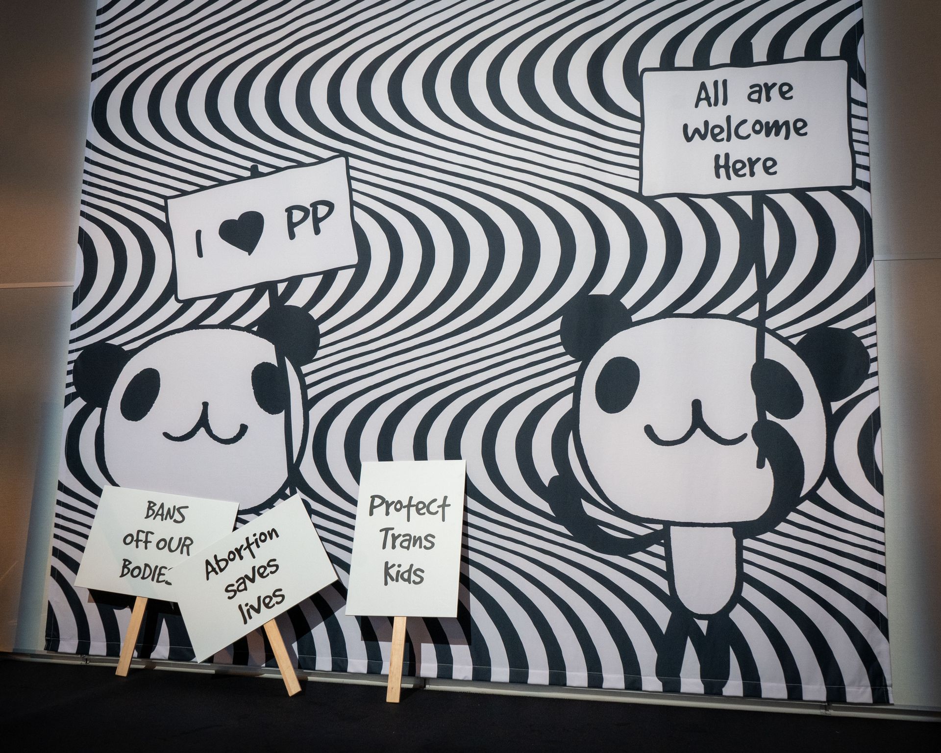 Planned Parenthood Event at The Glasshouse - photo of two pandas holding signs in front of a wall that says all are welcome here