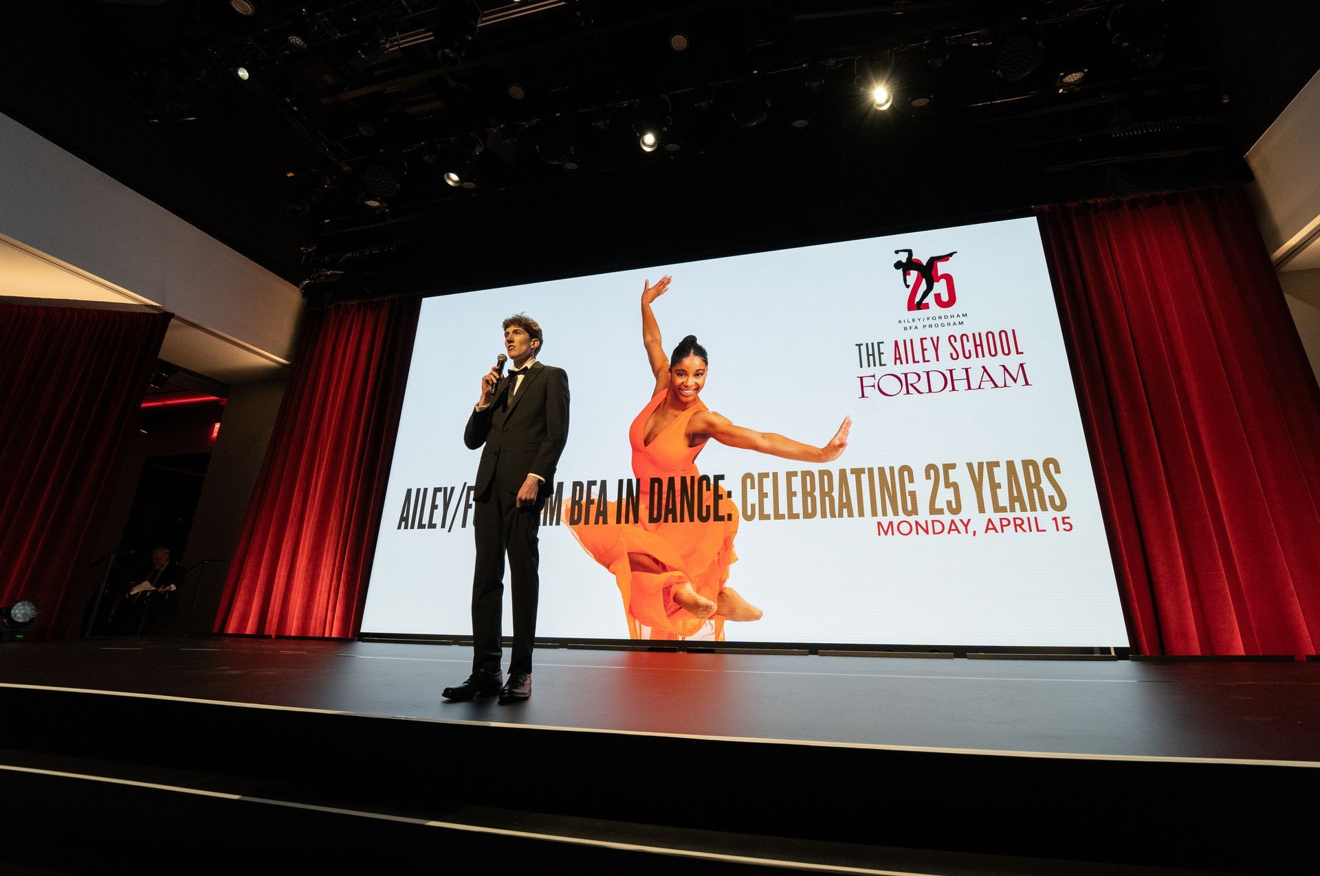 A man is standing on a stage in front of a large screen.