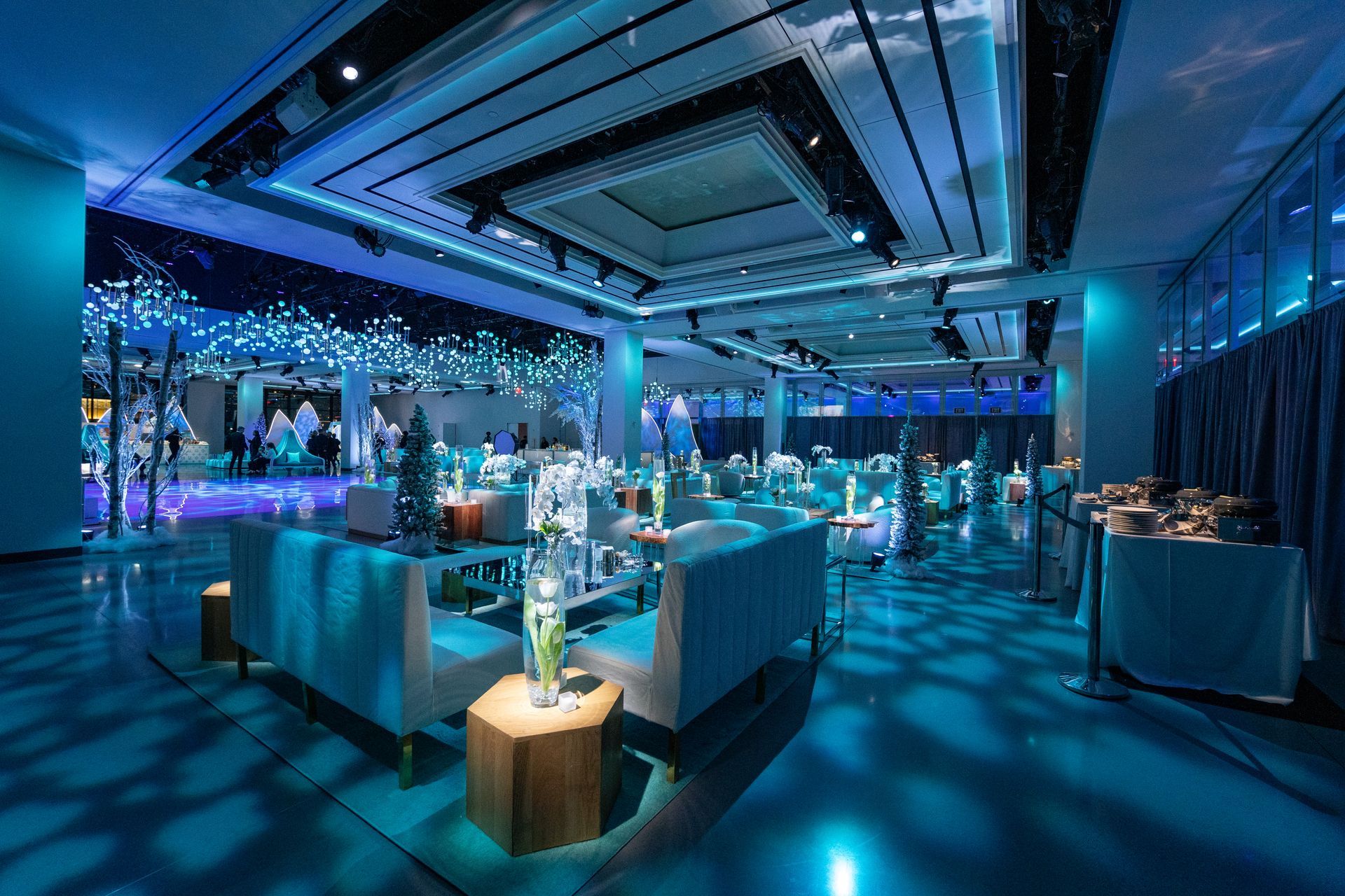 Elegant event space with blue lighting, seating, and tables; decorated with decorative elements.