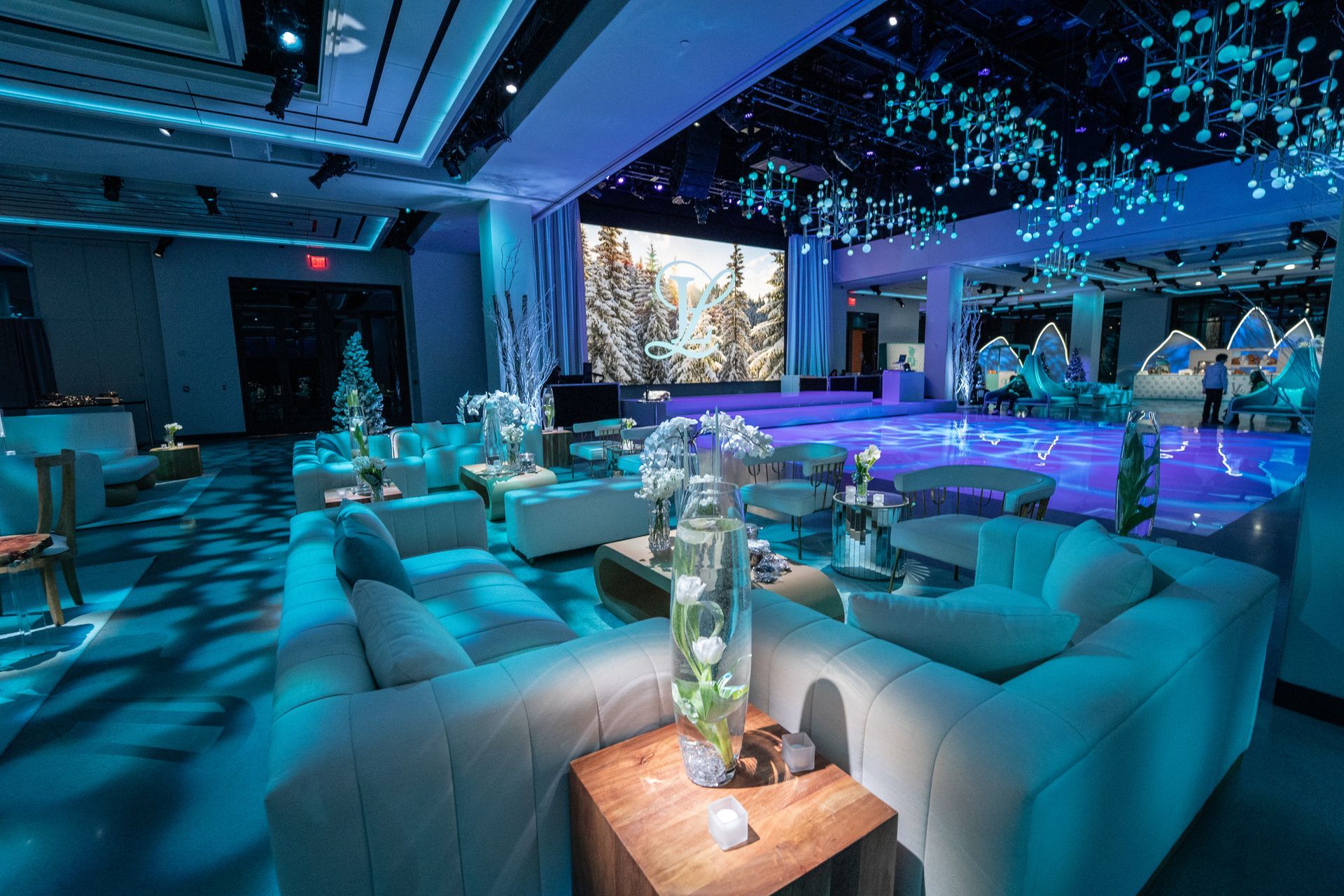 Luxurious event space with blue lighting, white couches, and a stage displaying a snowy scene.