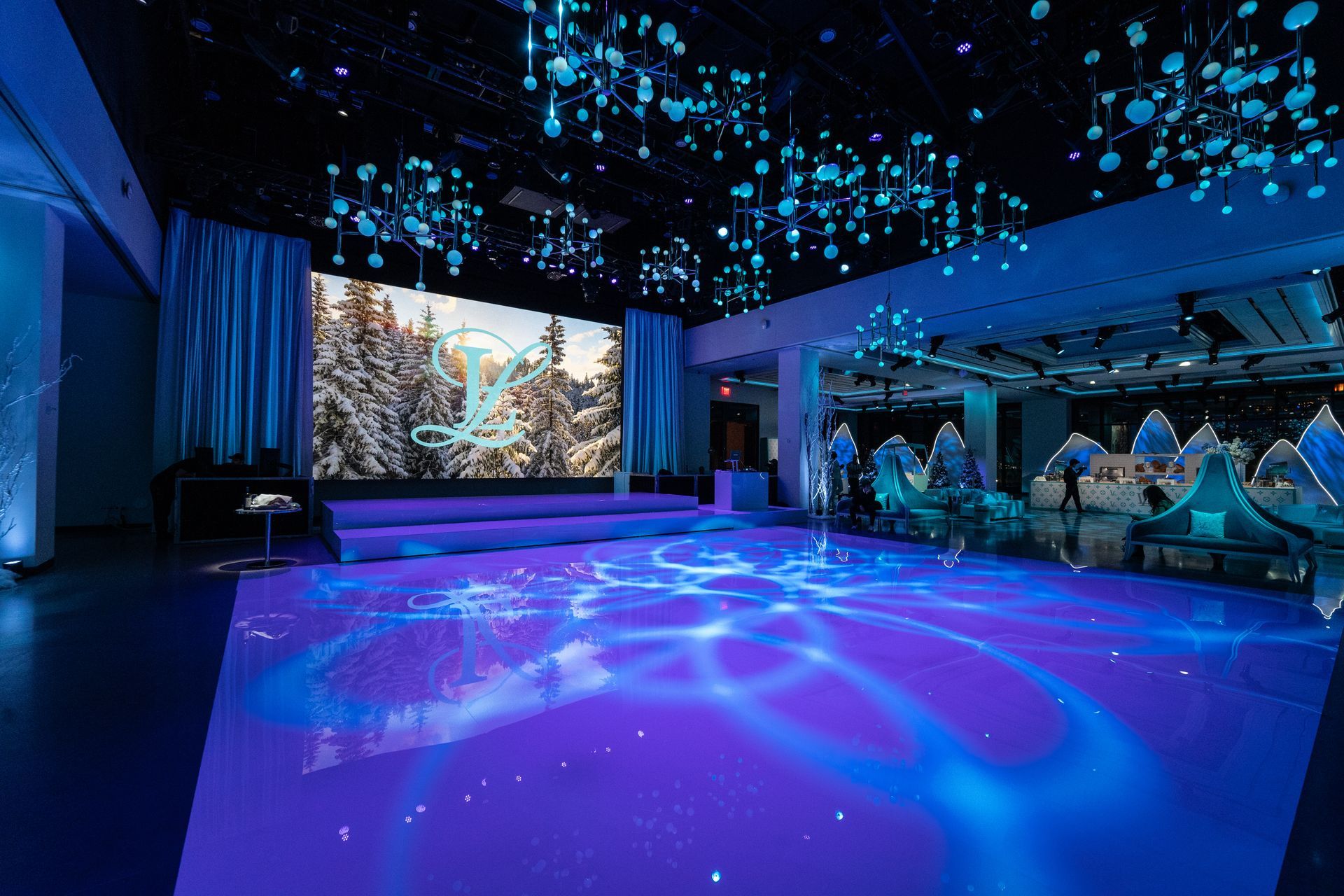 A blue-lit event space with a stage, projected winter scene, and water-like floor lighting.
