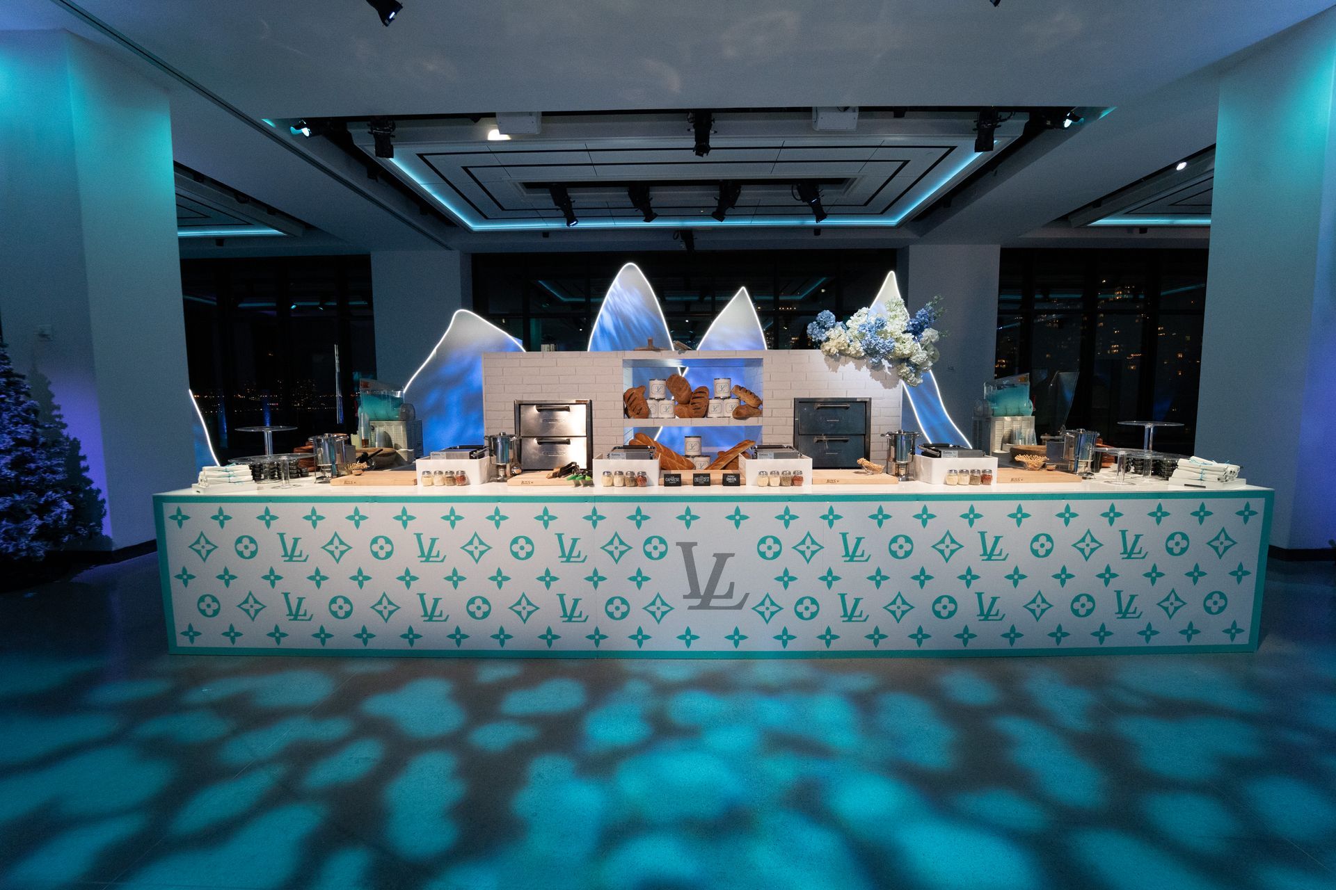 A Louis Vuitton event setup with a long counter displaying desserts, set against a blue, winter-themed background.