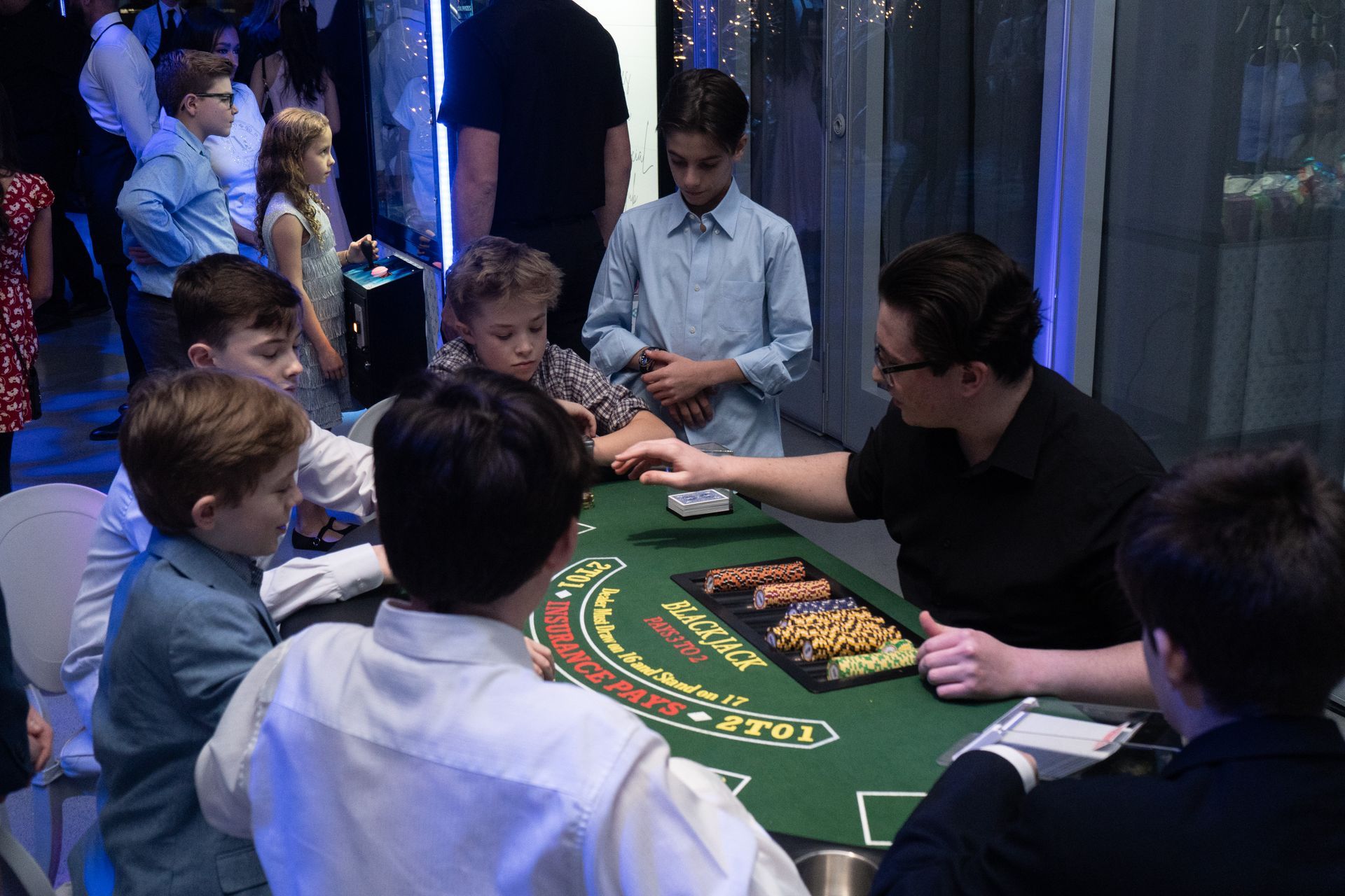 Children playing blackjack at a party, overseen by a man in a dark shirt.