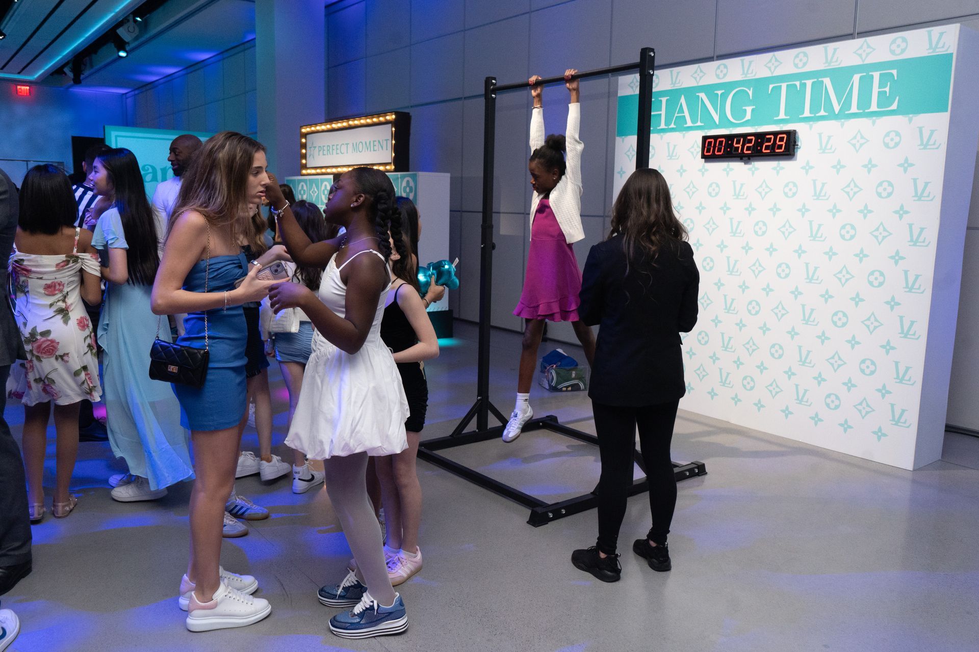 A girl hanging from a pull-up bar at an event, with others watching.