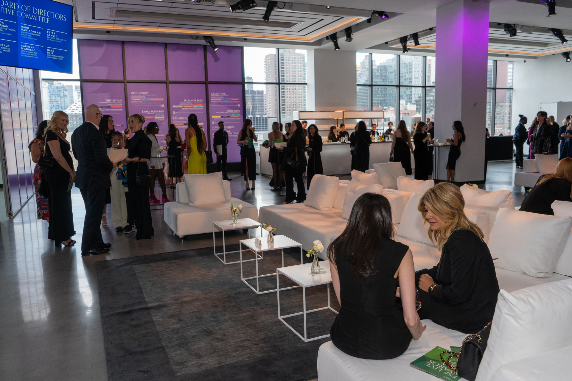 A group of people are standing and sitting in a large room.