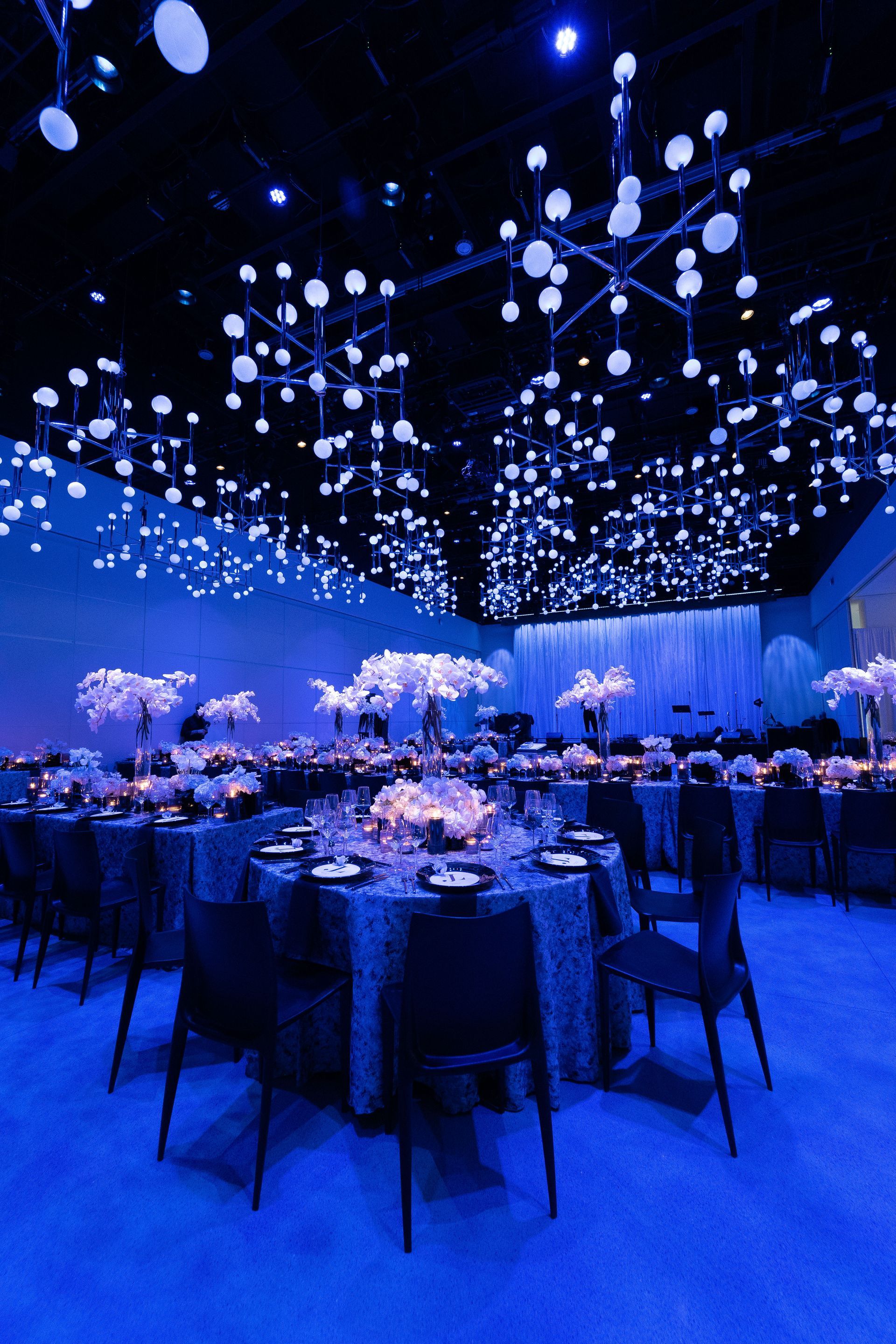 tables and chairs are set up in a large room with blue lights hanging from the ceiling