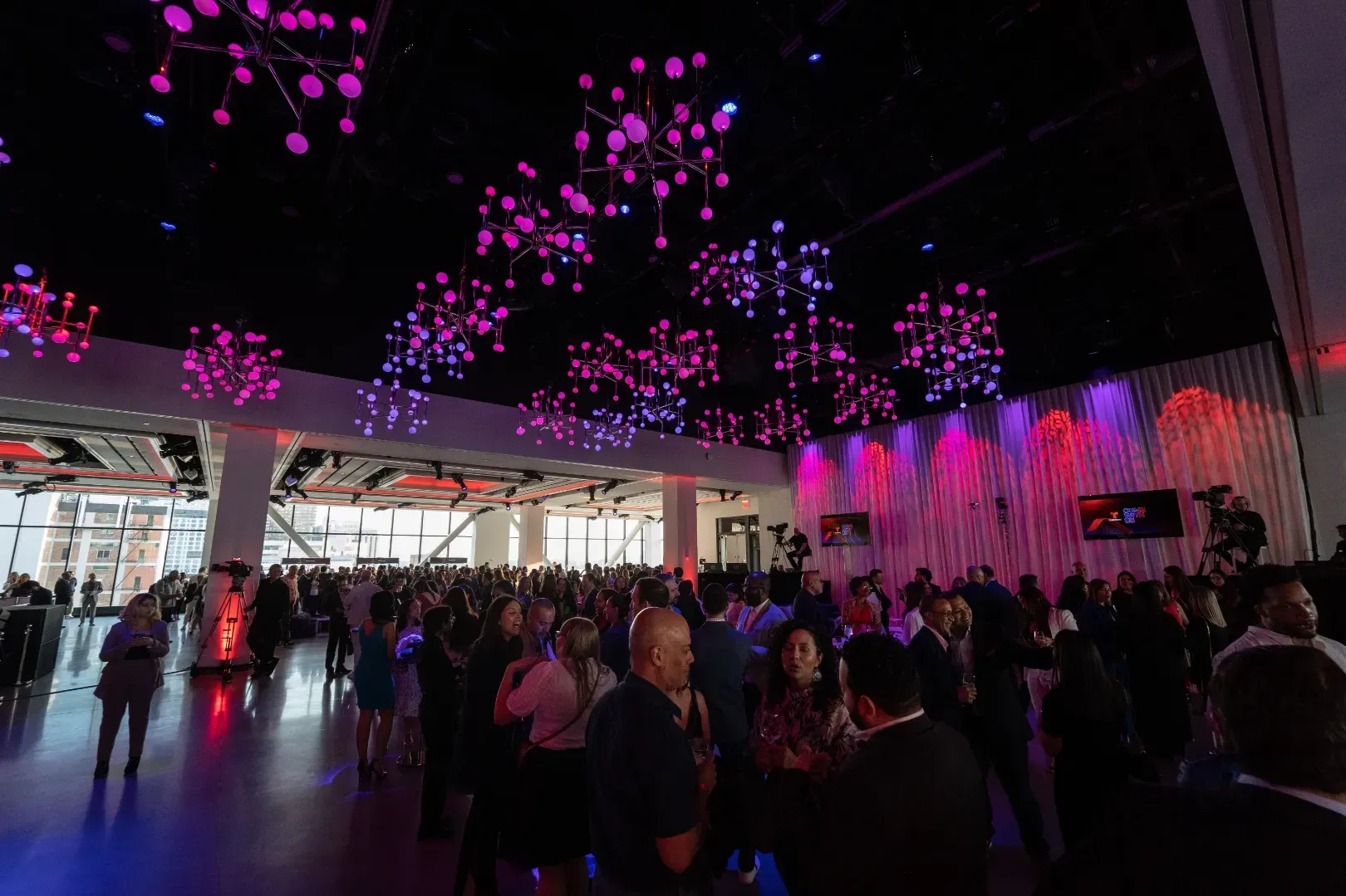 A large group of people are standing in a room with a lot of lights on the ceiling.