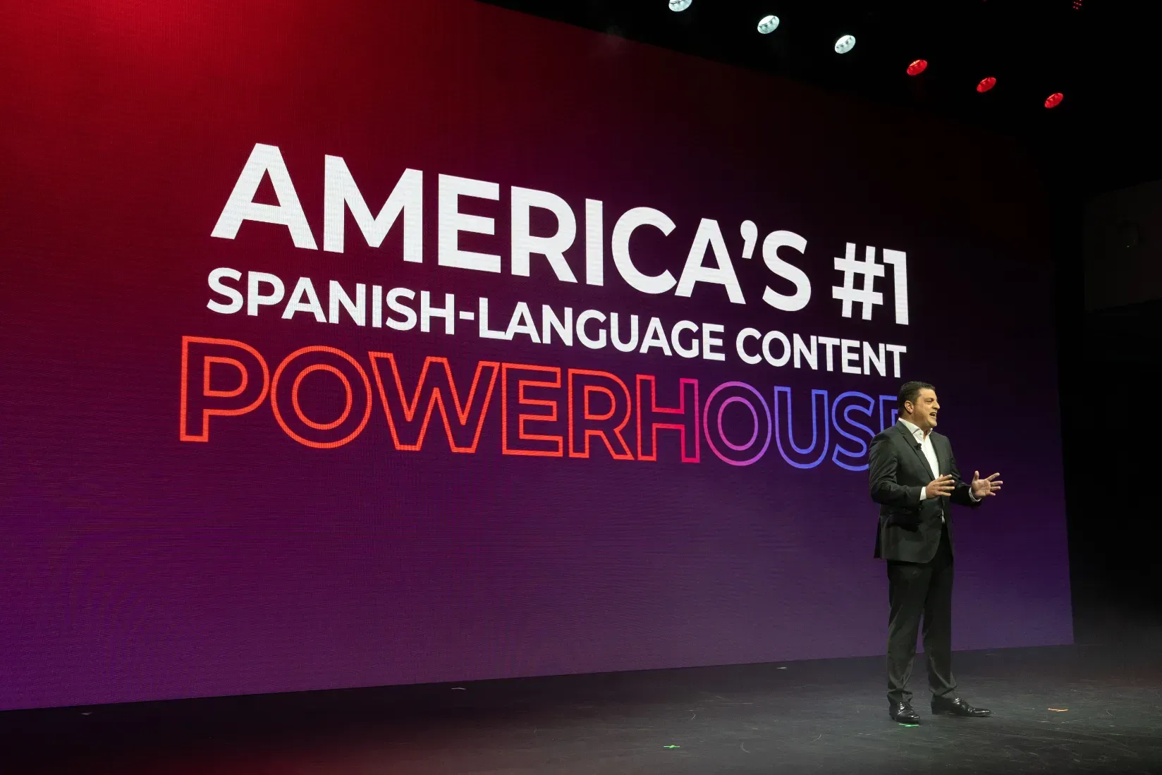 A man is standing in front of a large screen that says america 's # 1 spanish language content powerhouse