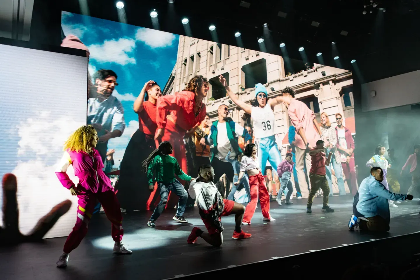 A group of people are dancing on a stage in front of a large screen.