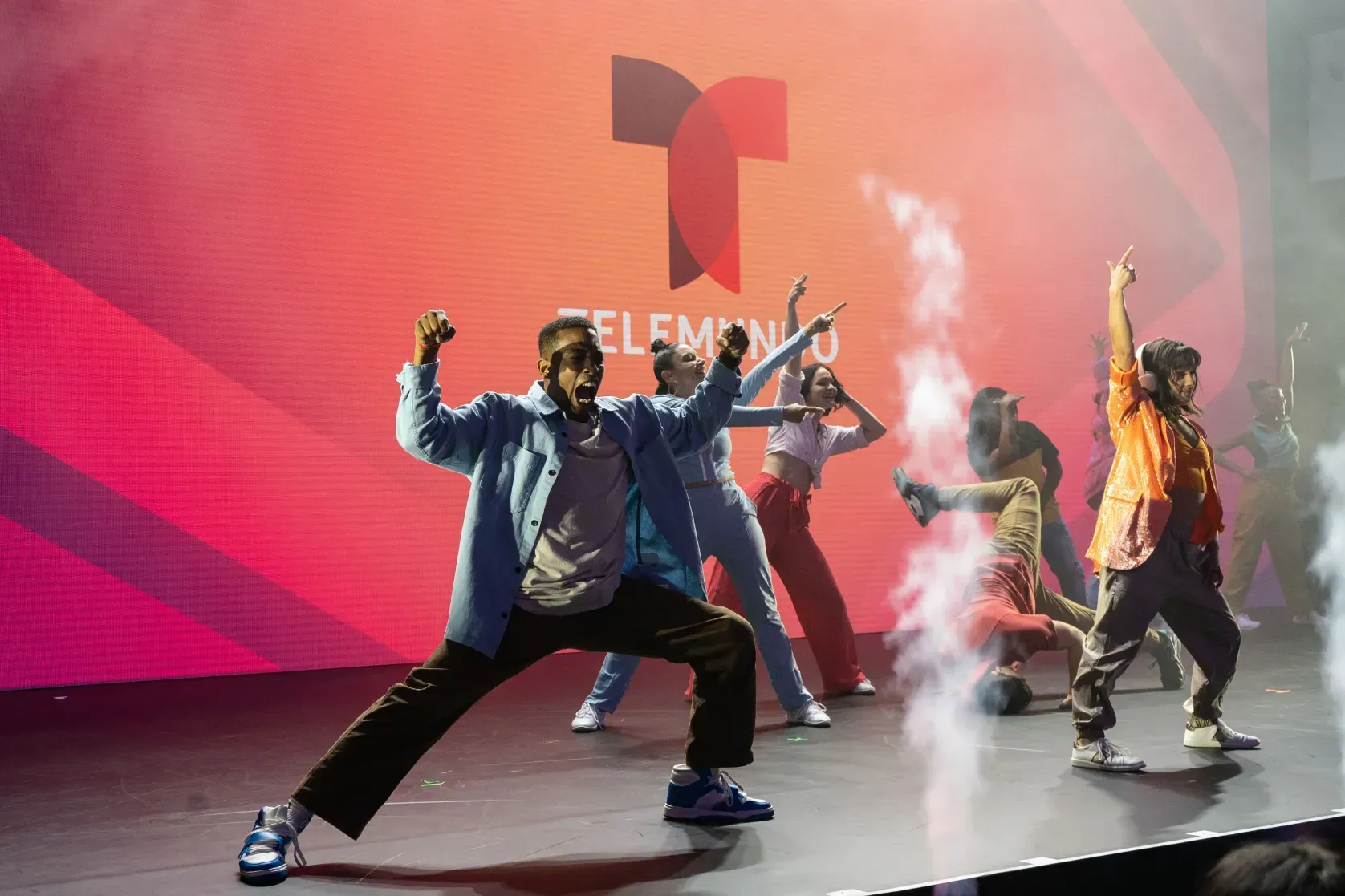 A group of people are dancing on a stage in front of a telemundo logo.
