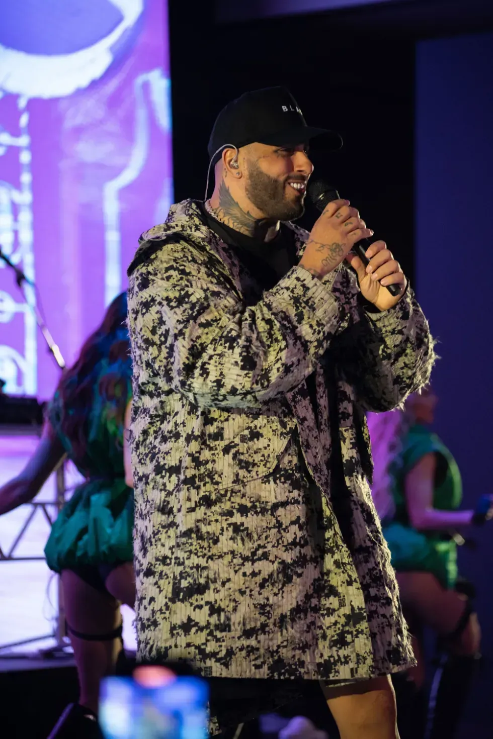 A man in a camouflage jacket is singing into a microphone on a stage.