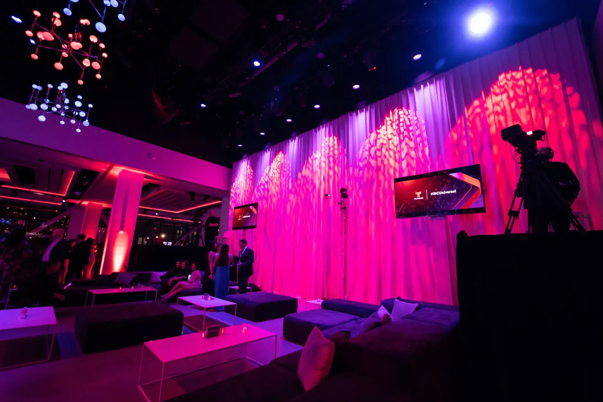 A camera is sitting in front of a pink wall in a dark room.