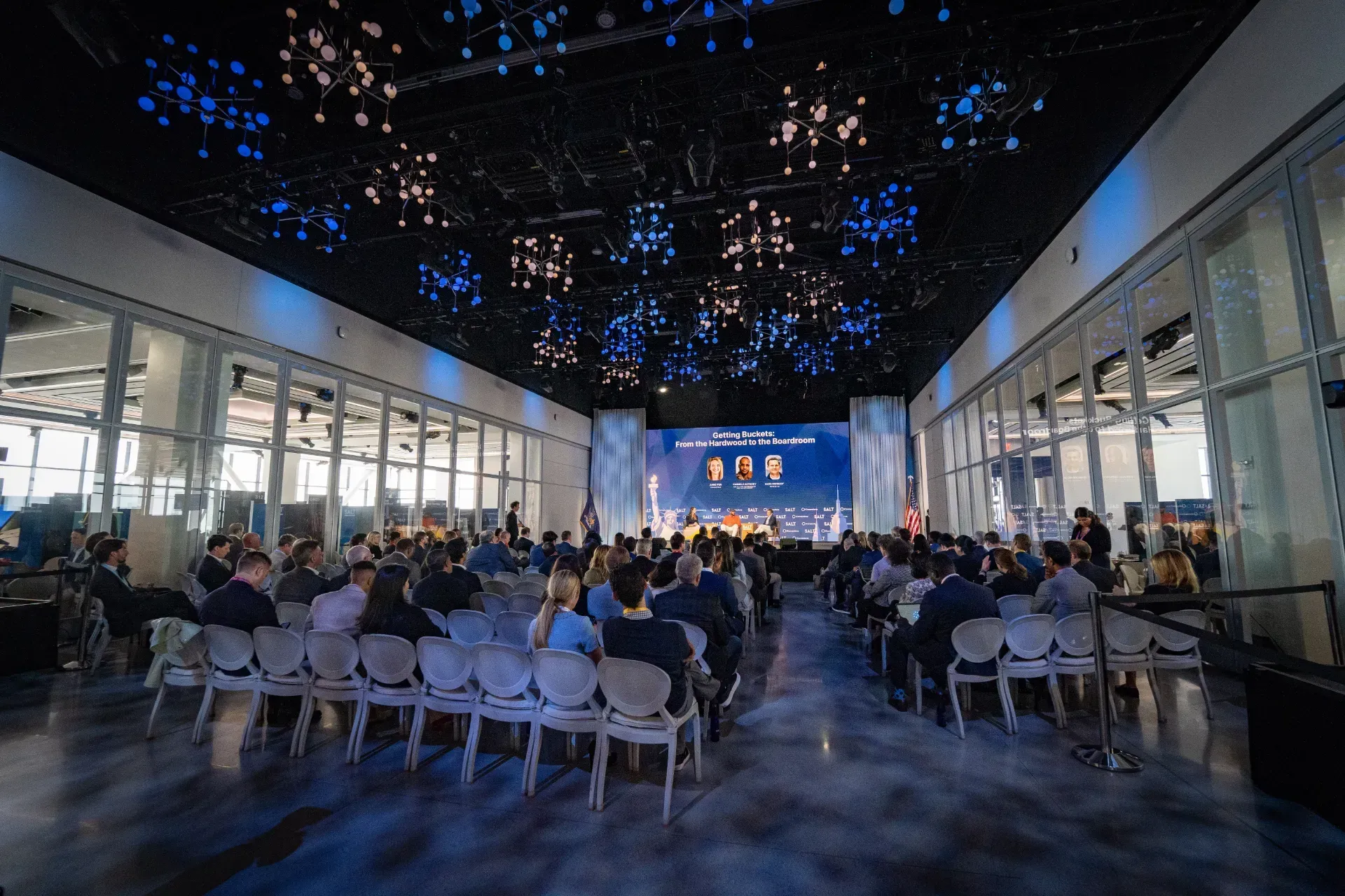 A large room filled with people sitting in chairs in front of a stage.