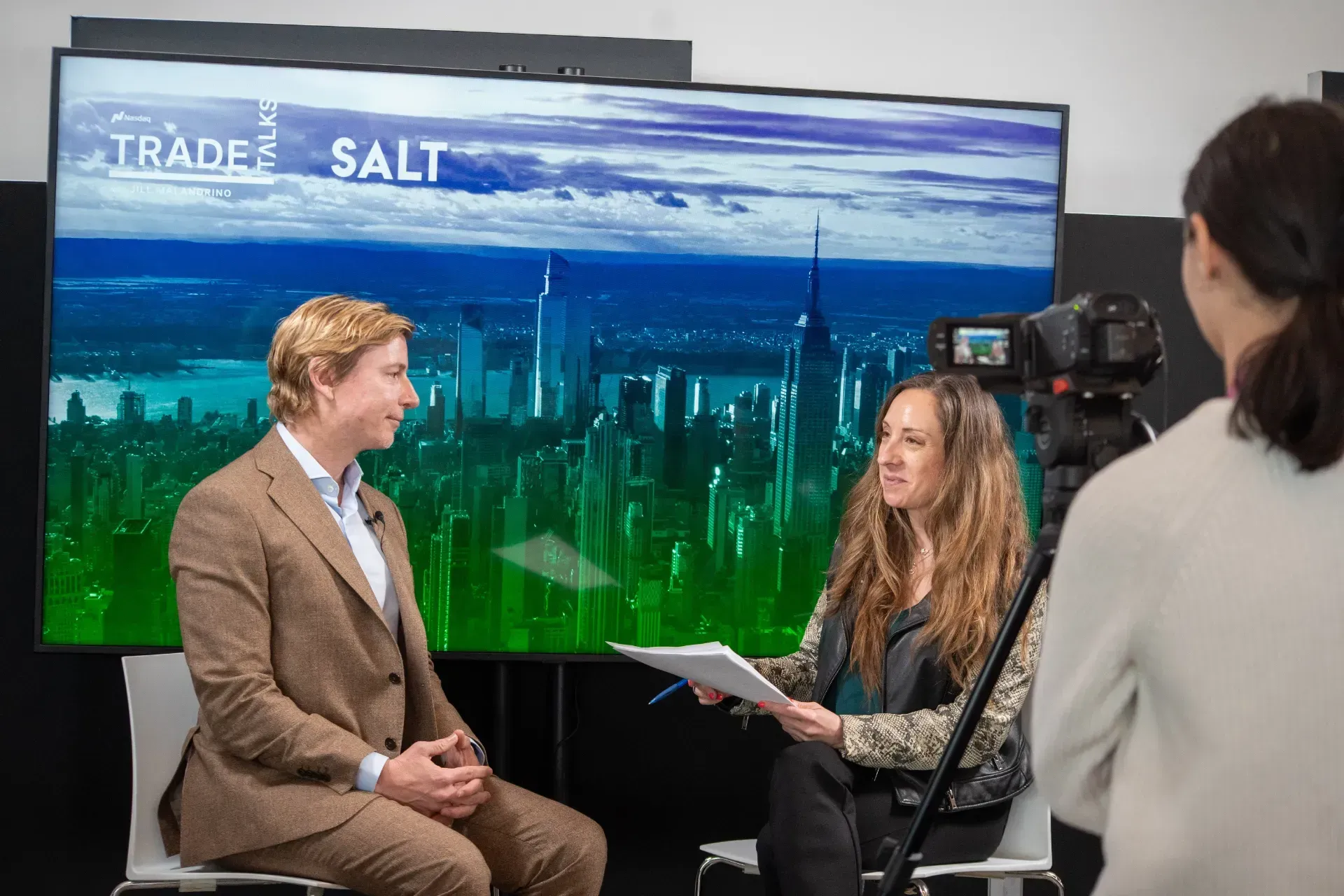 A man in a suit is being interviewed by a woman in front of a large screen.