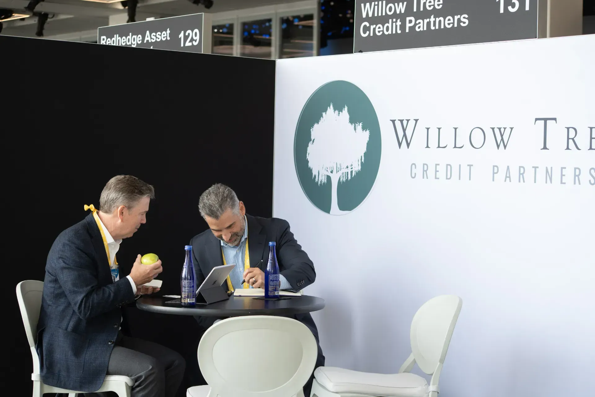 Two men are sitting at a table in front of a sign that says willow tree credit partners