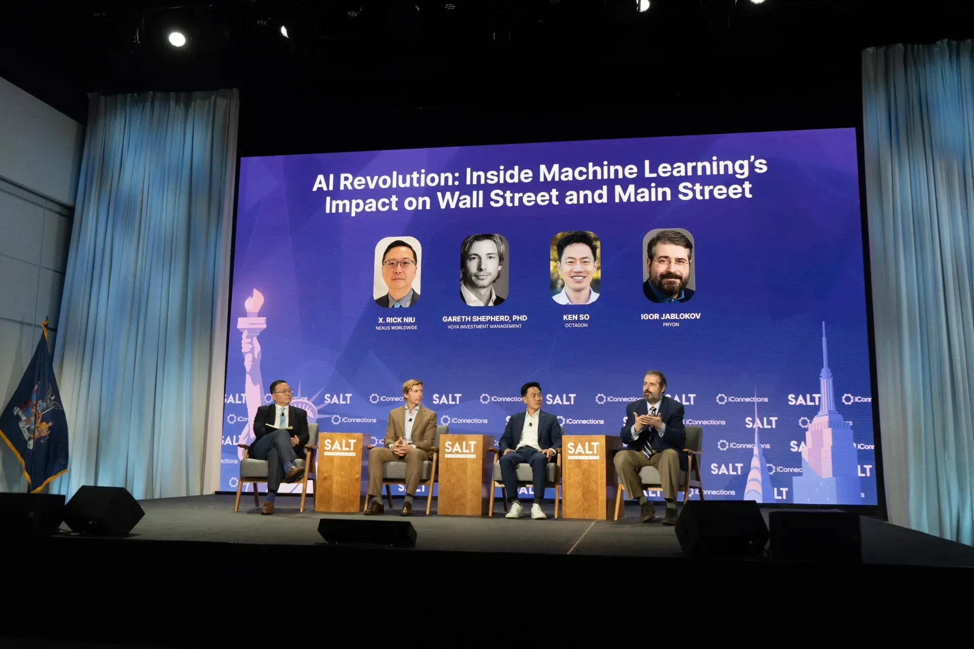 A group of people are sitting on a stage in front of a large screen.