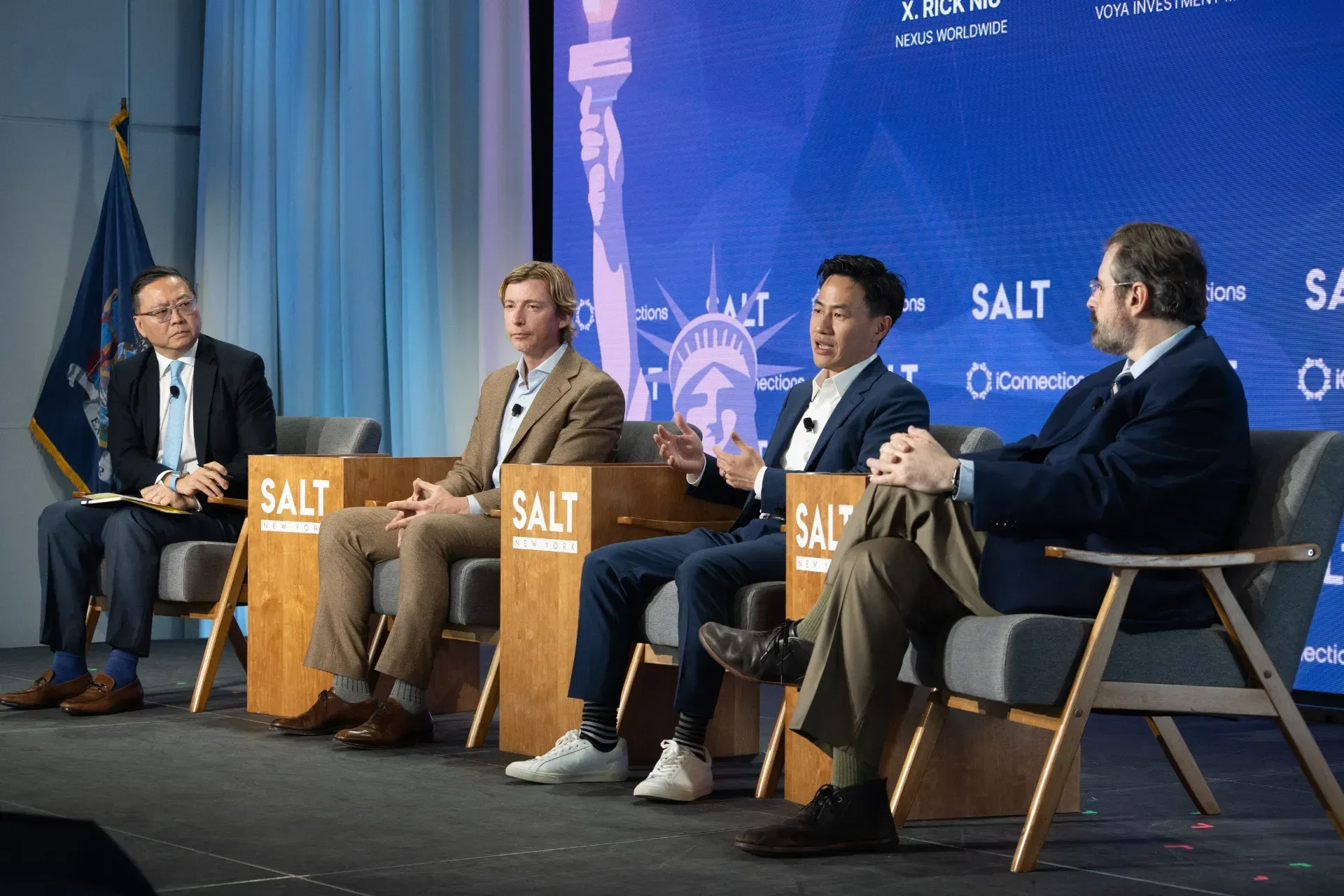 A group of men are sitting in chairs on a stage at a conference.