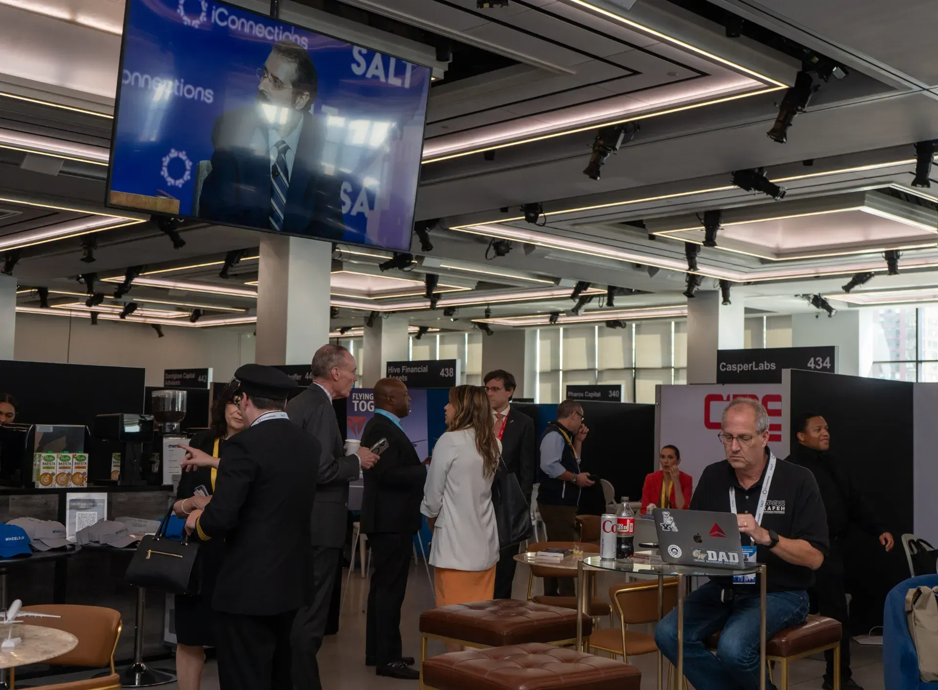 A group of people are standing in a room with a large screen hanging from the ceiling.
