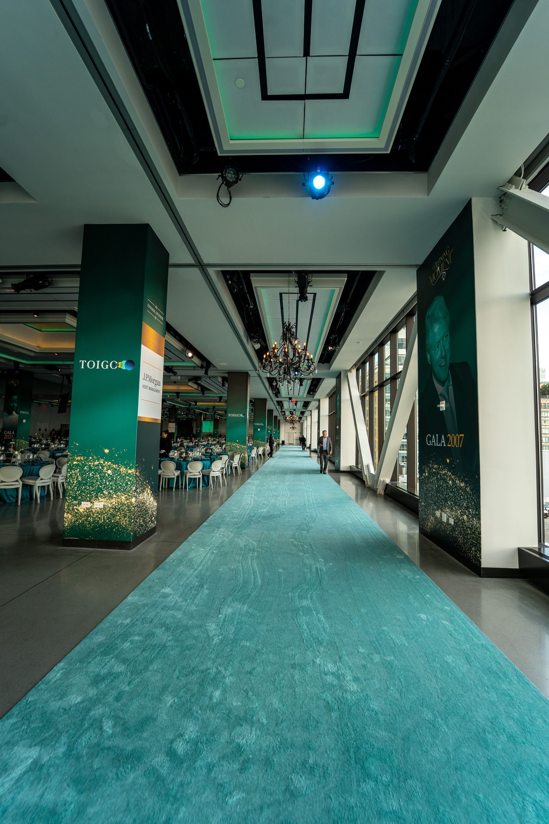 A long hallway with a blue carpet and a projector on the ceiling.