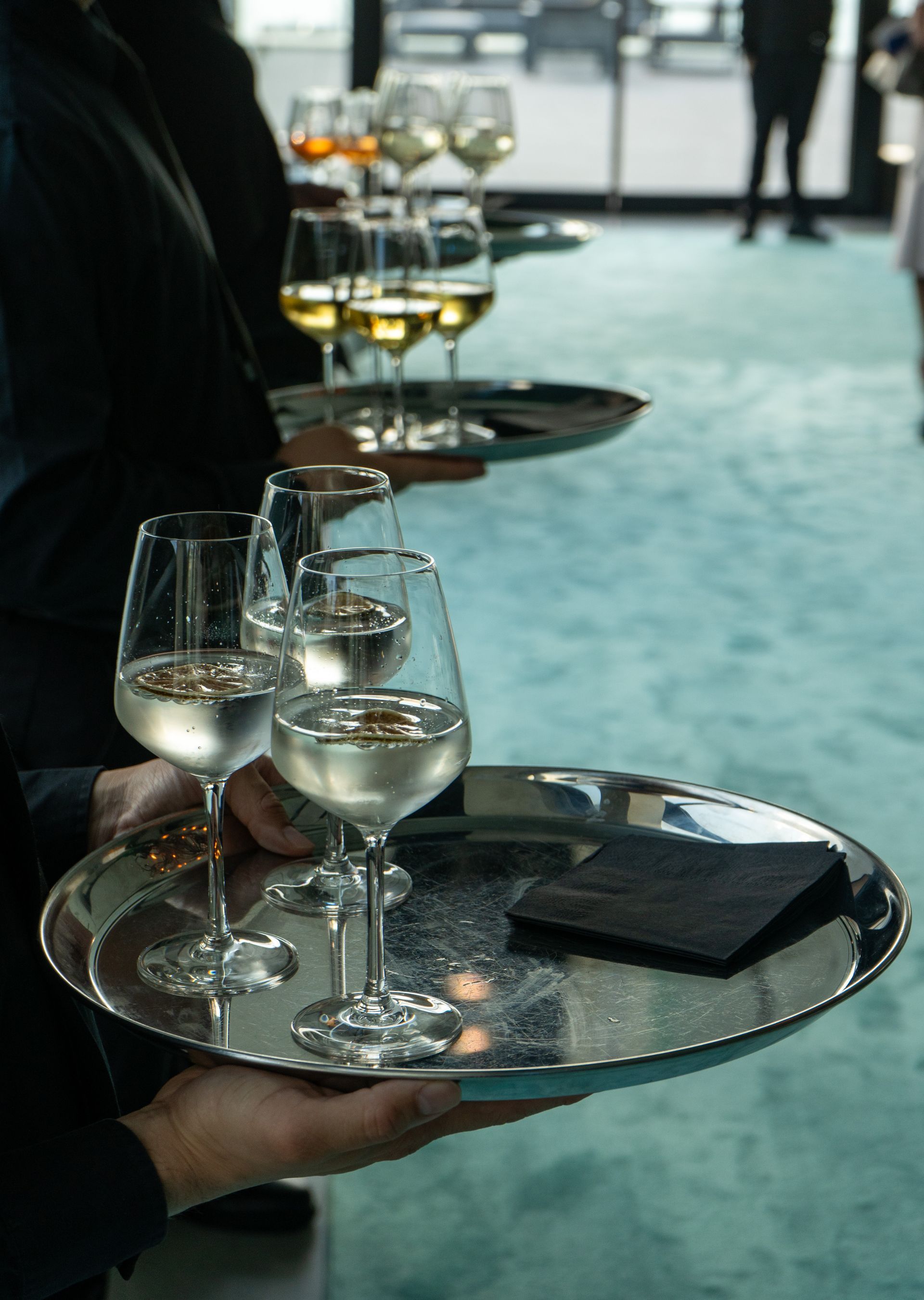 A person is holding a silver tray with wine glasses on it.