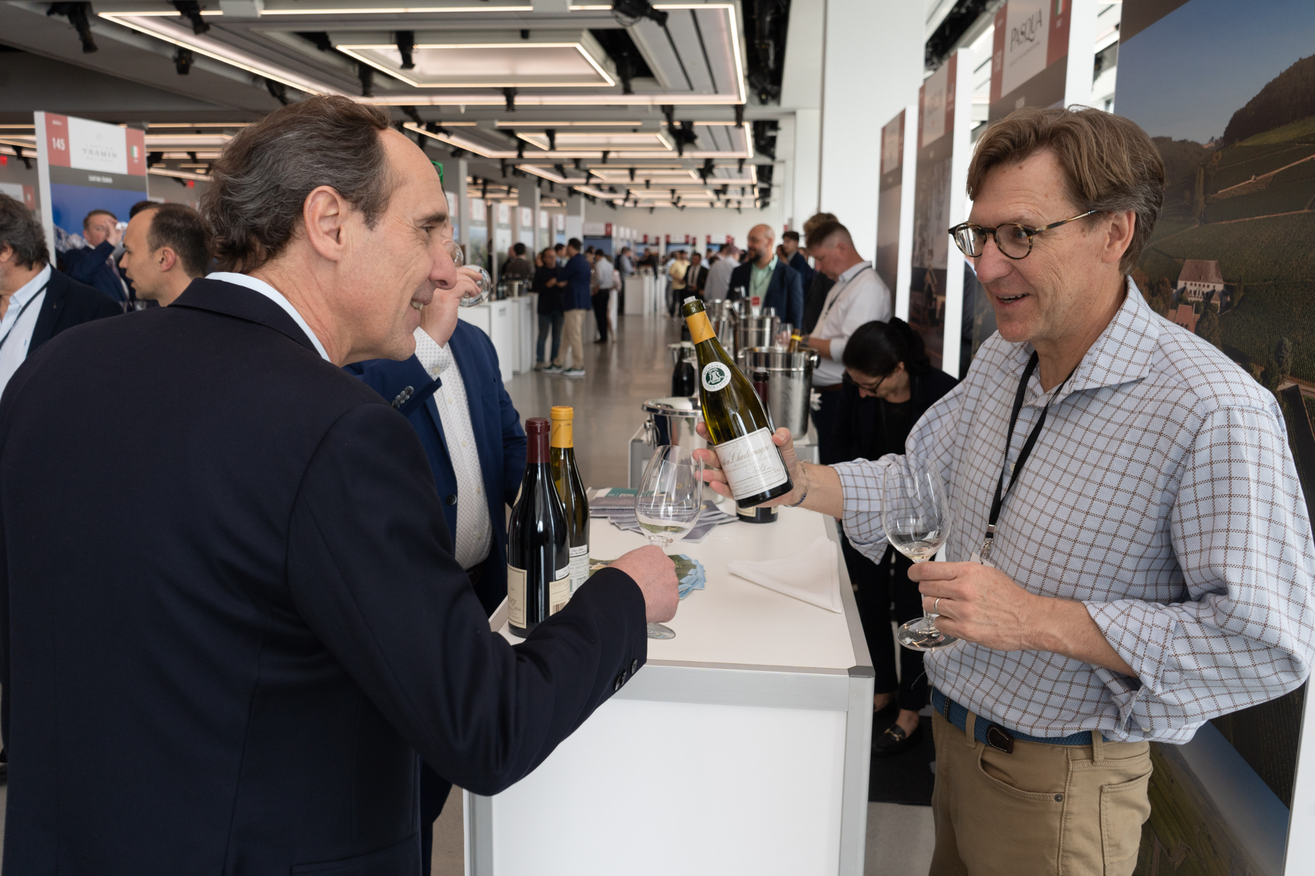 A man is pouring wine into another man 's glass at a wine tasting.