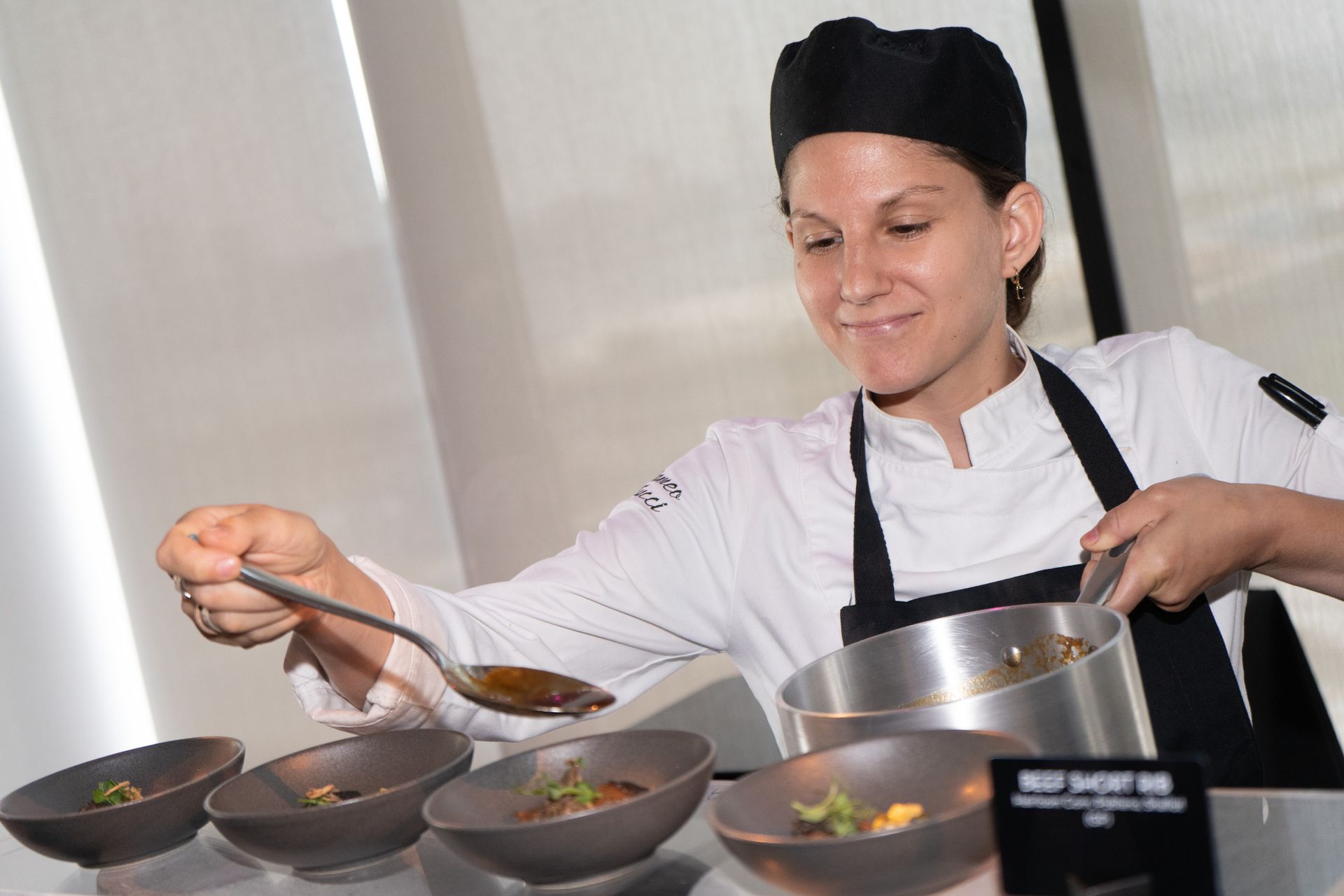 A woman in a chef 's uniform is preparing food in bowls.