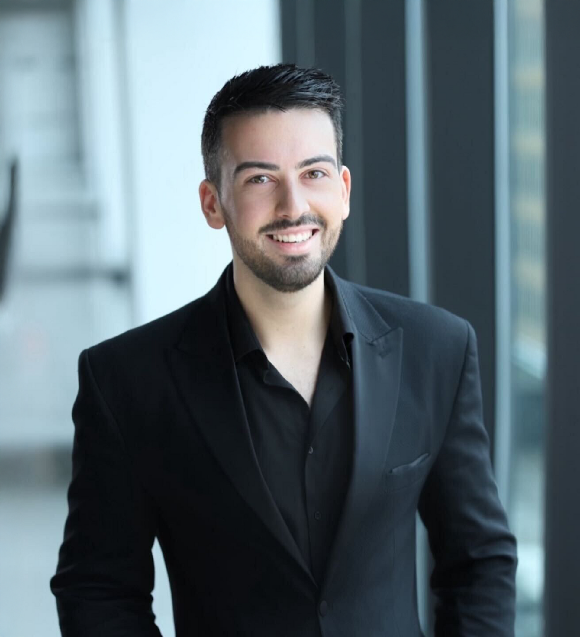 A man in a black suit and black shirt is smiling for the camera.