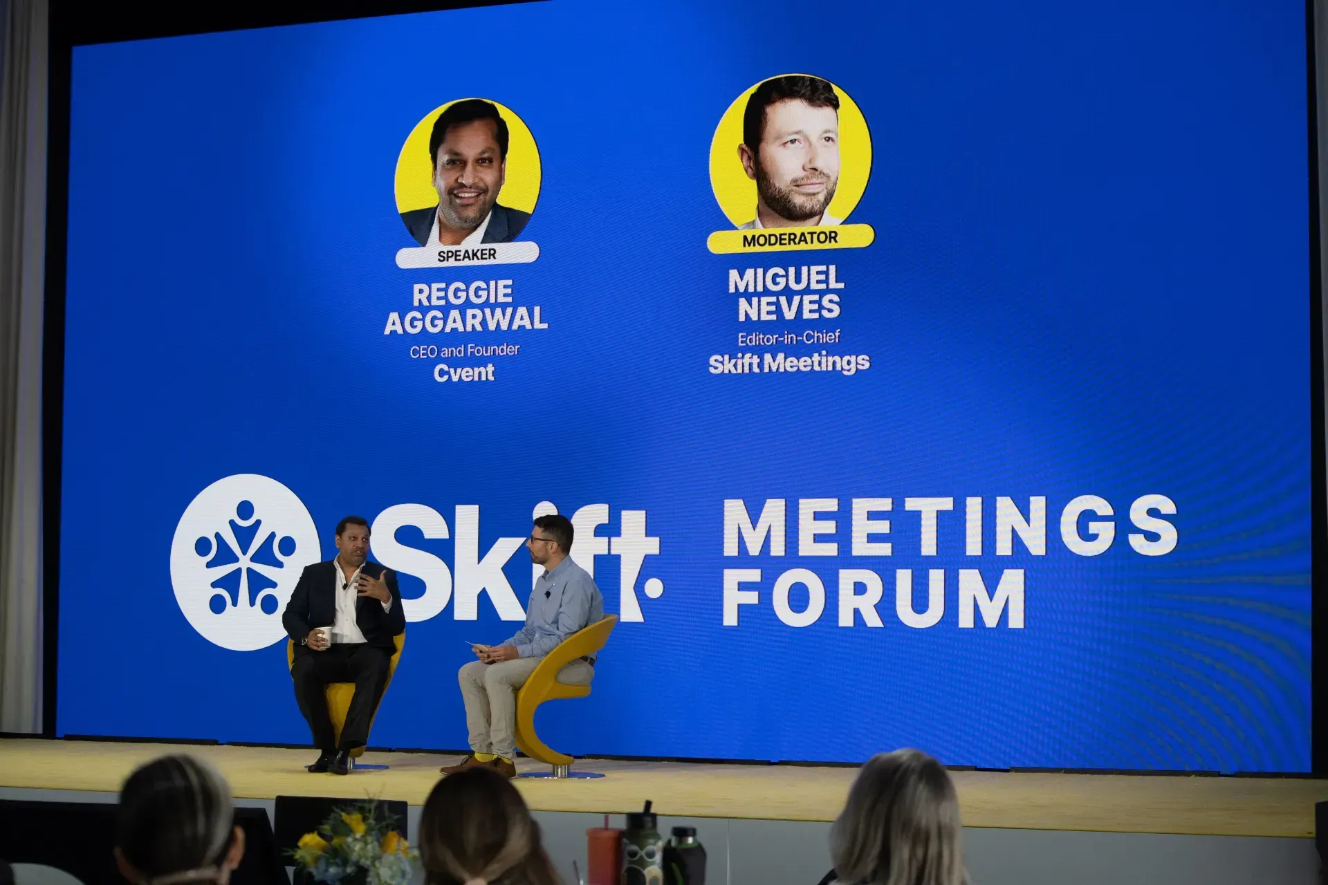 A group of people are sitting in front of a large screen that says meetings forum.