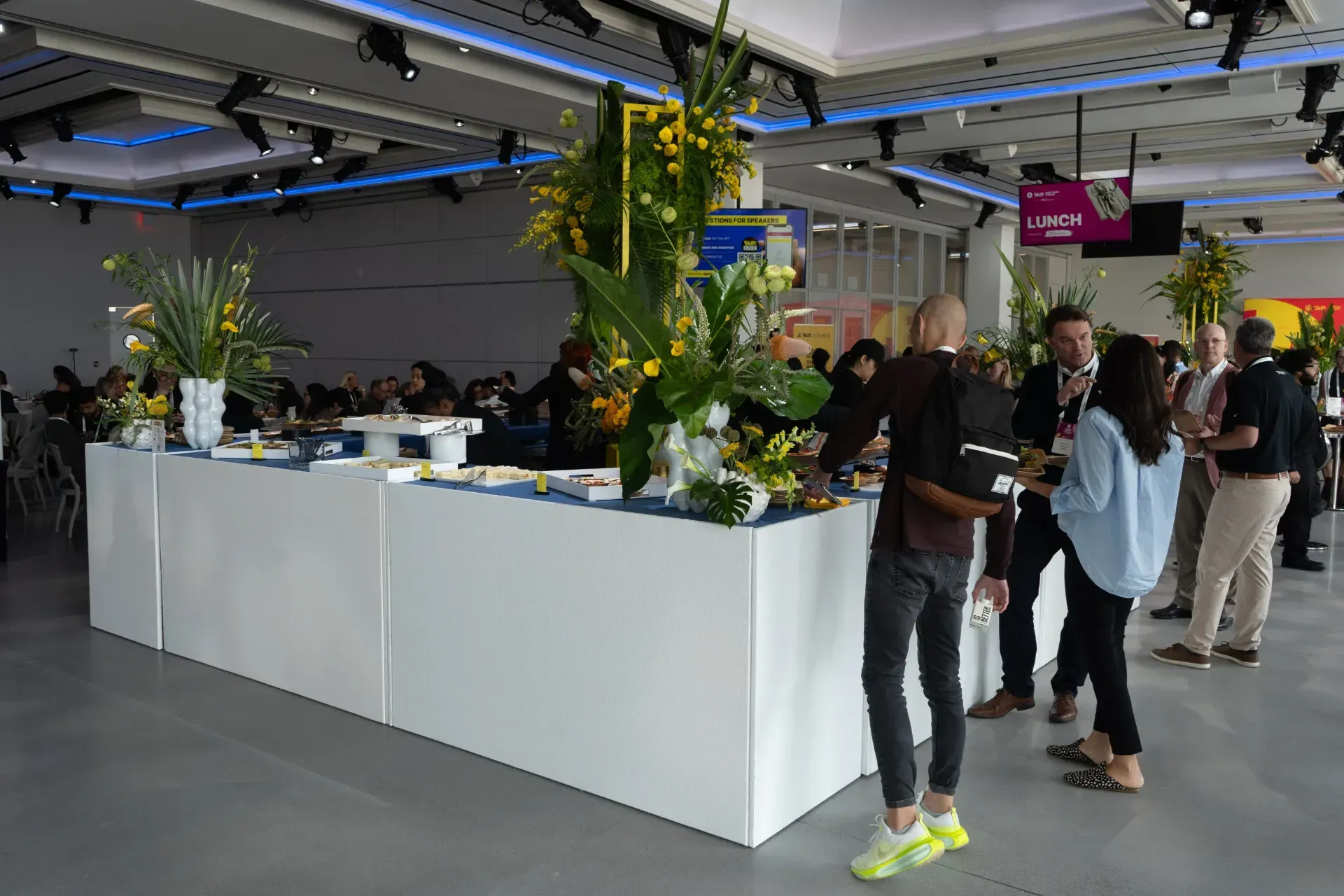 A group of people are standing around a long white table in a large room.