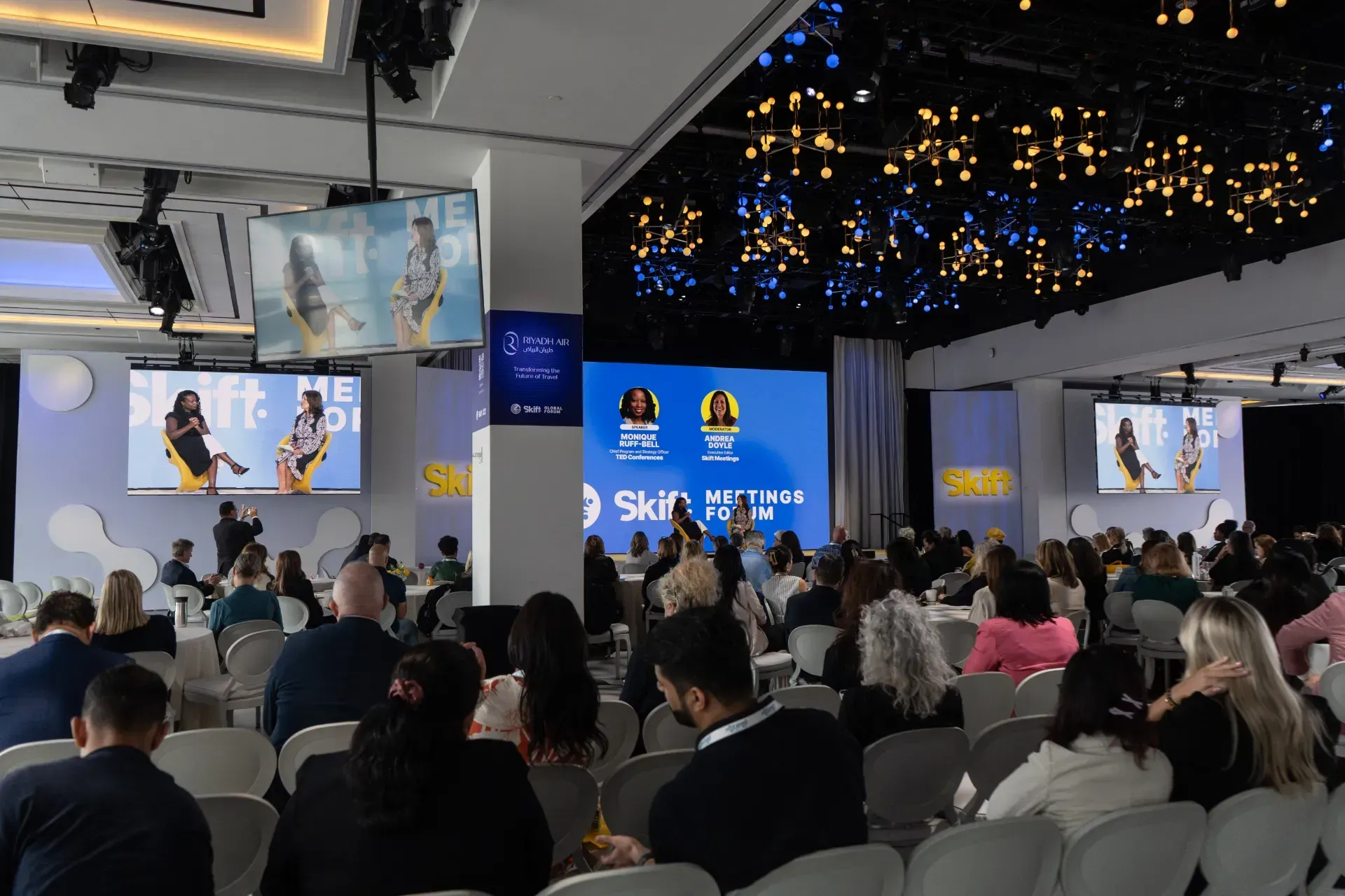 A large group of people are sitting in front of a large screen.