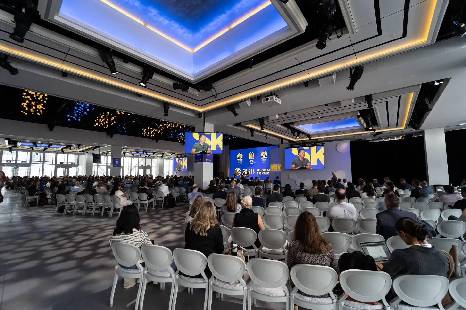 A large room filled with people sitting in chairs watching a presentation.